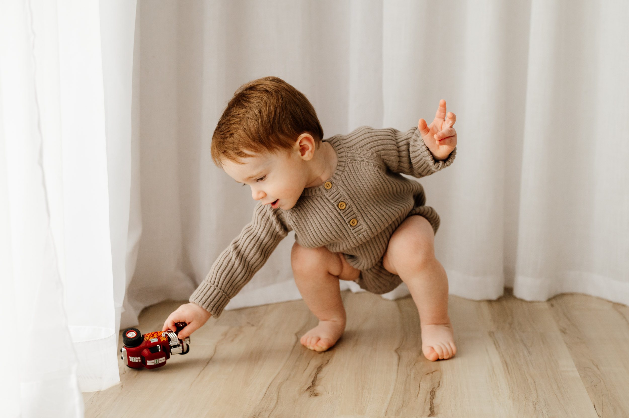 a young boy squatting down and reaching out to pick up his toy truck during a toddler milestone photoshoot