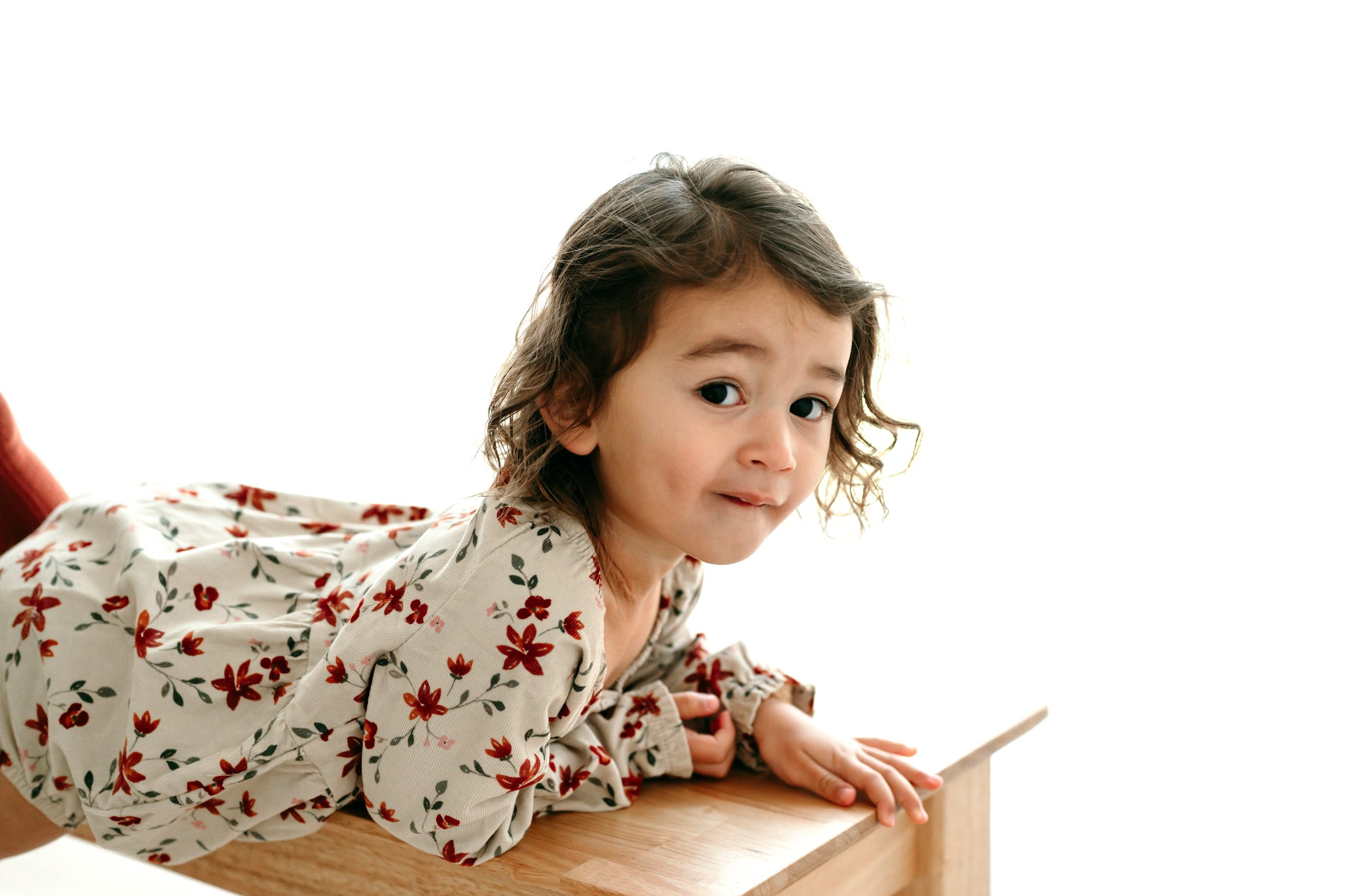 a backlit picture of a young girl laying on a wooden bench and looking directly at the camera during a toddler milestone photoshoot