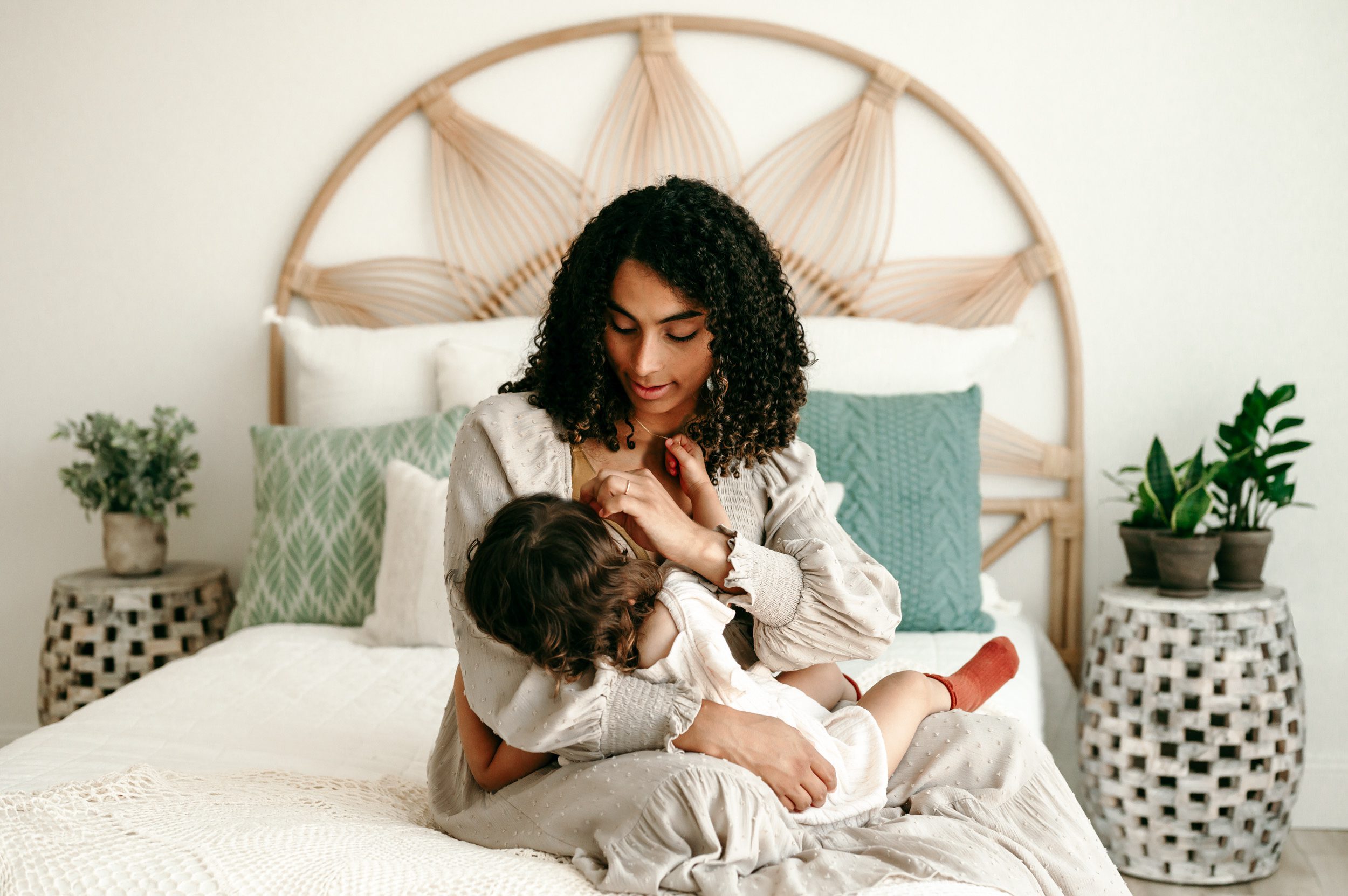 a mom sitting on a bed nursing her toddler and gently brushing her little girl's hair out of her face during a toddler milestone photo session