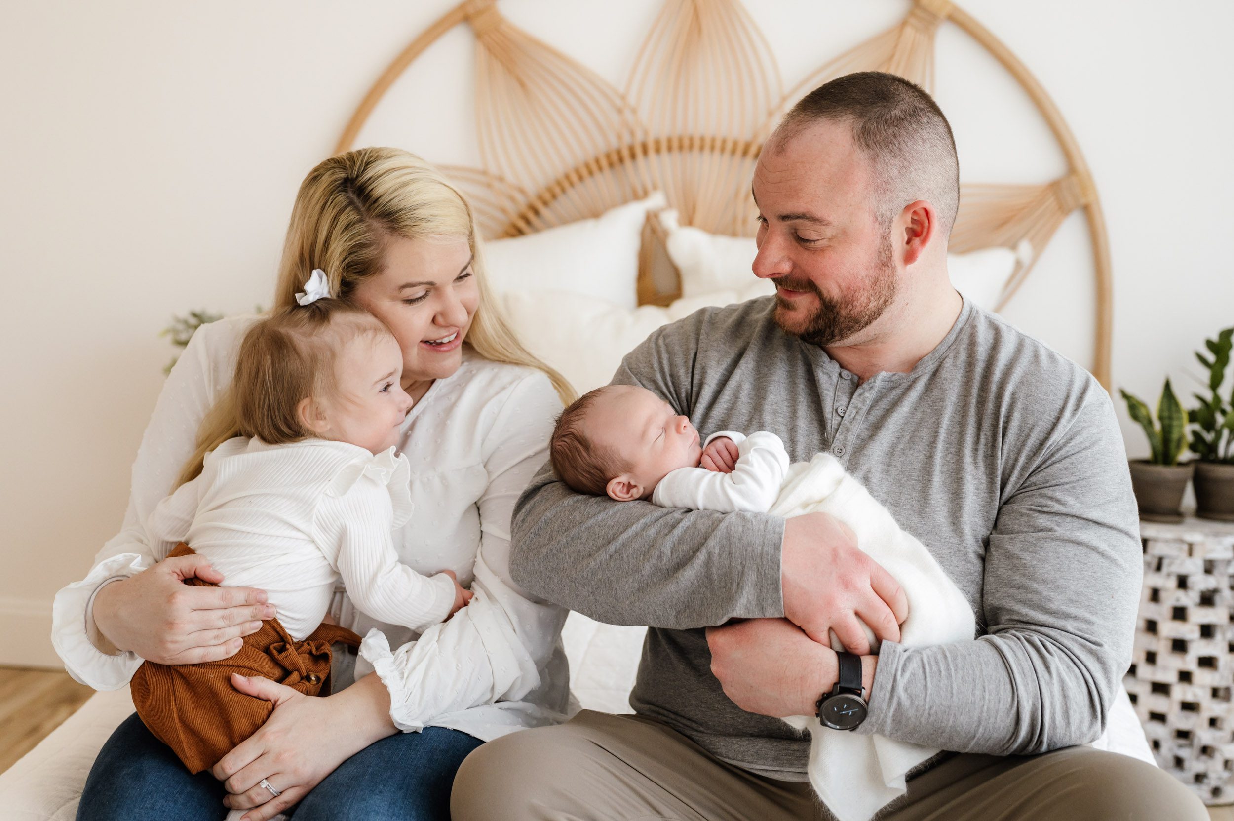 a family of four sitting on a bed and snuggling with their new baby boy during a lifestyle newborn photo session