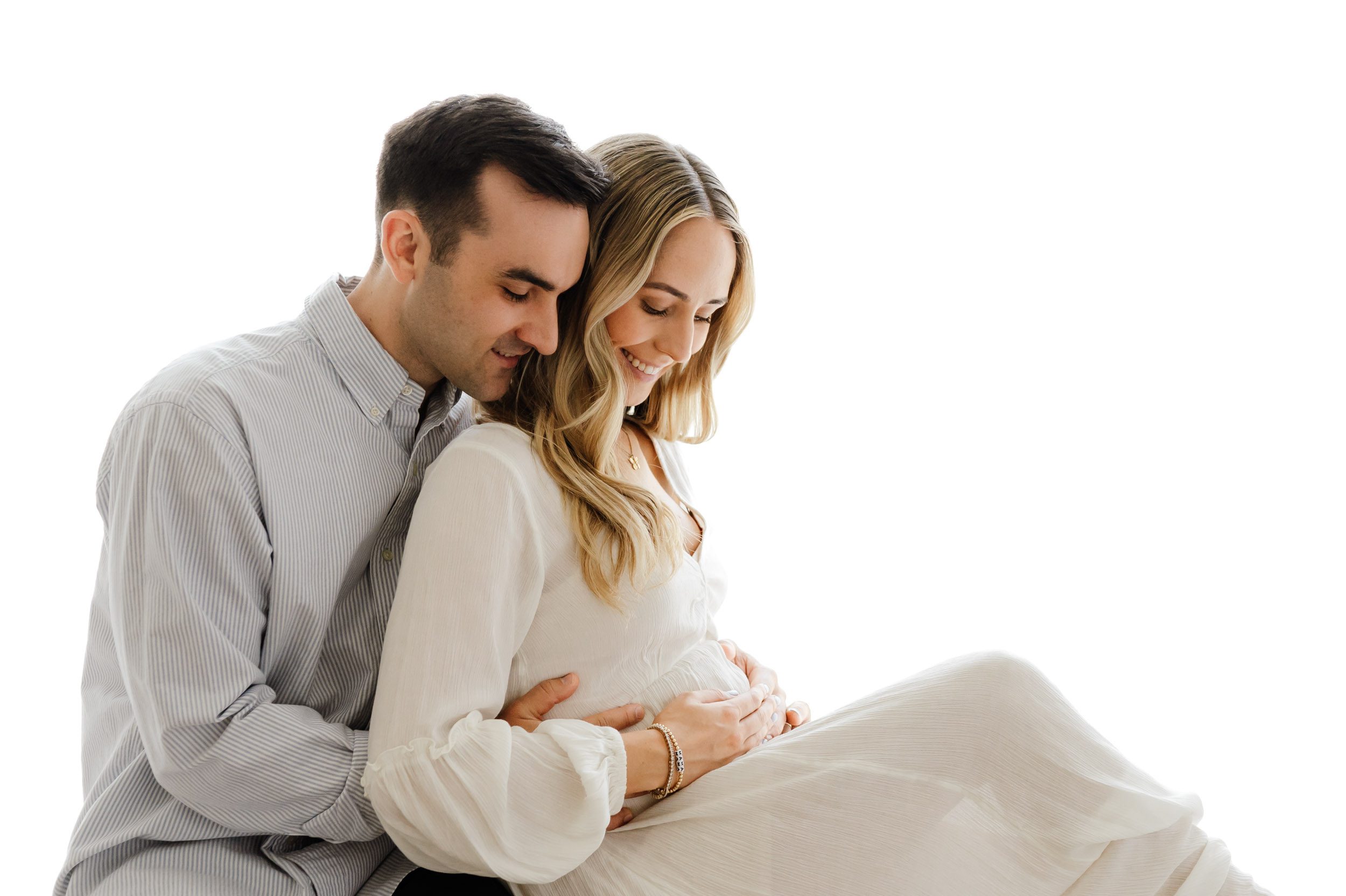 a backlit photo of expecting parents sitting on a bench and smiling as they both put their hands on mom's belly during a lifestyle maternity photos session