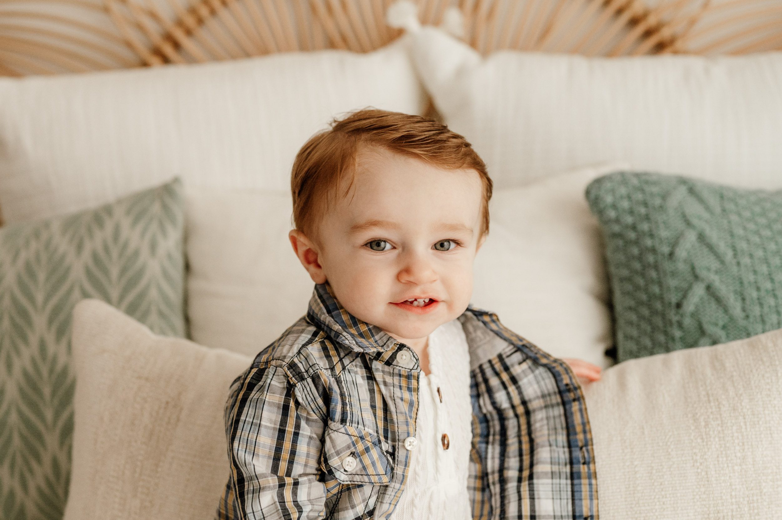 a young boy sitting on a bed and leaning against a pillow as he turns to look at the camera during a 1st birthday photoshoot