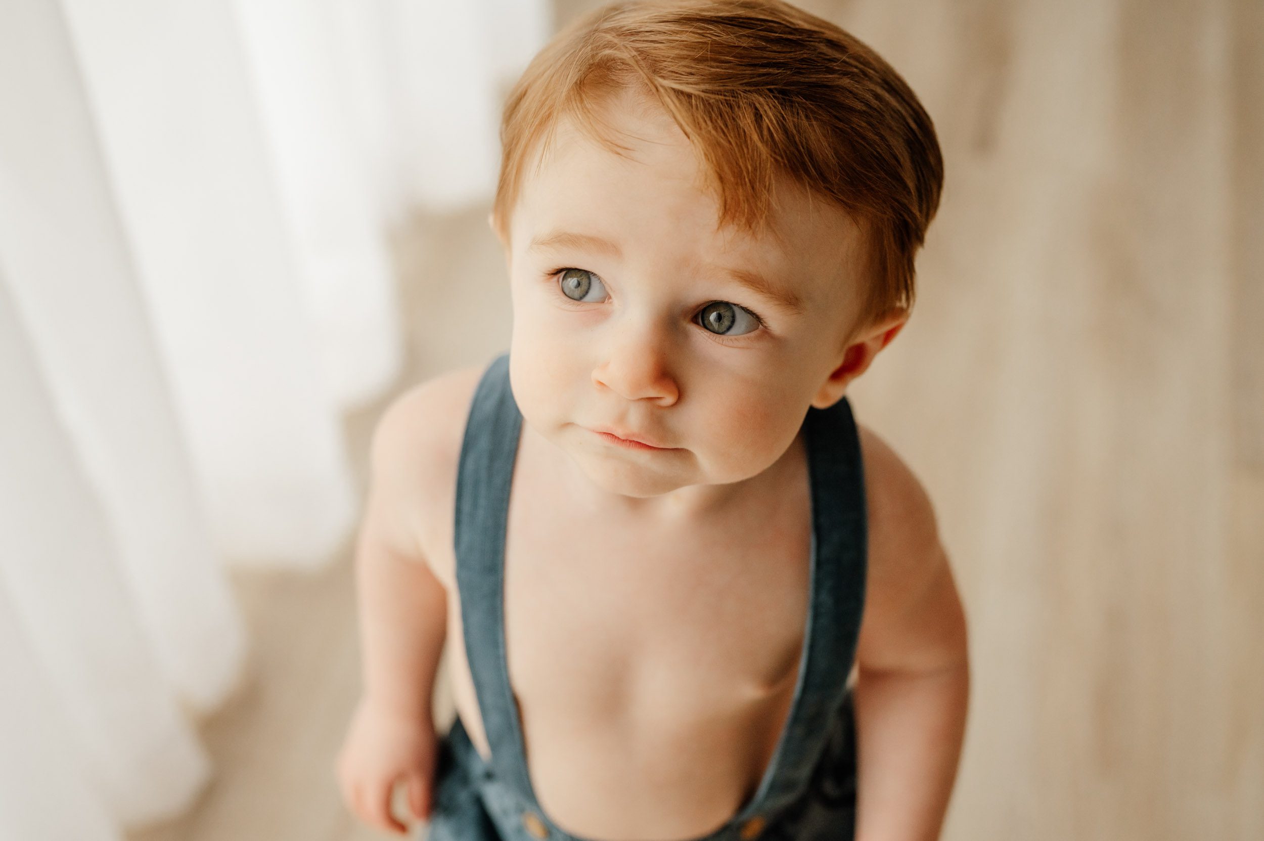 a picture of a young boy taken from above as he looks off to the side and the light catches the corner of his eyes during a 1st birthday photo session