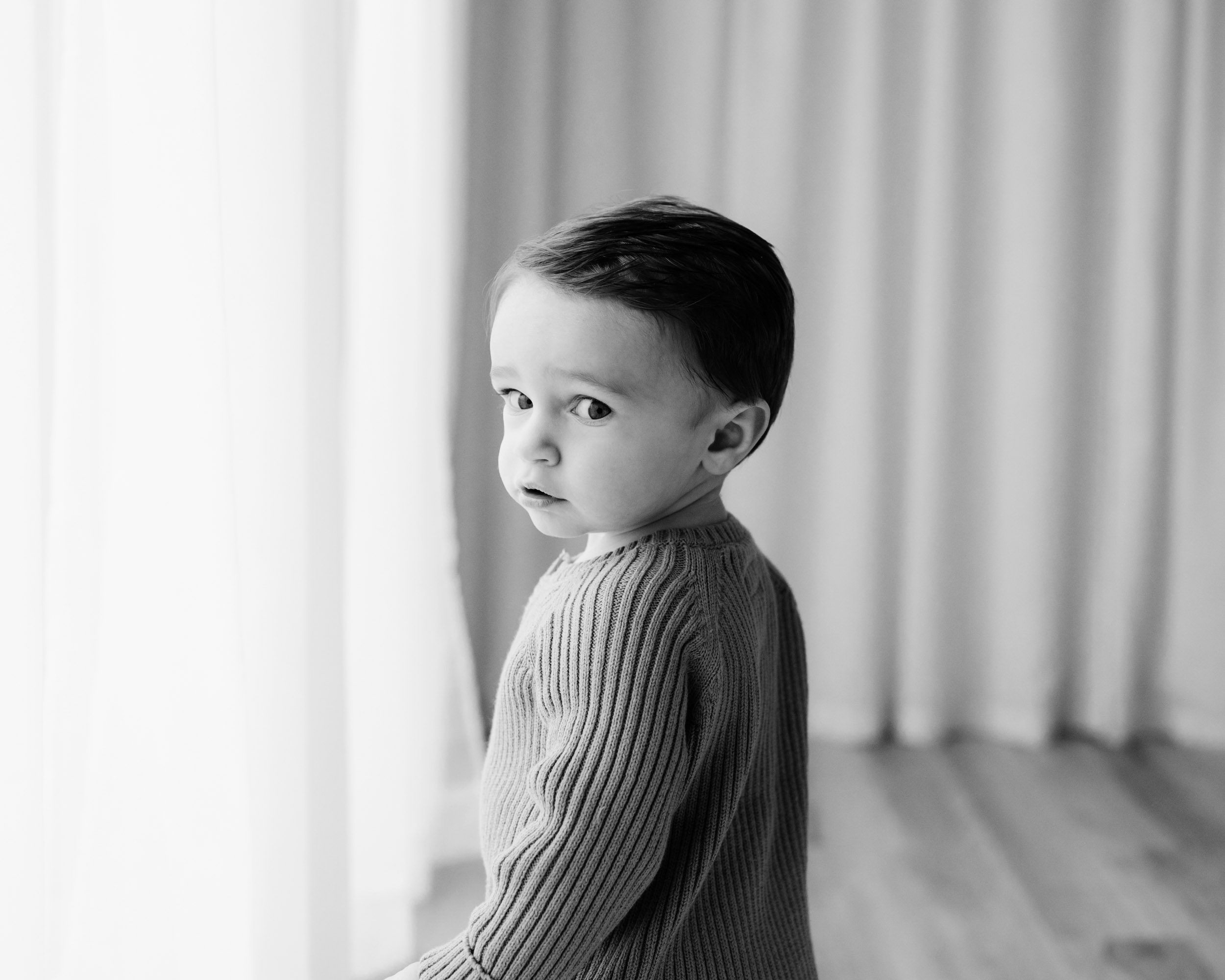 a black and white picture of a young boy turning around and looking at the camera out of the corner of his eyes 