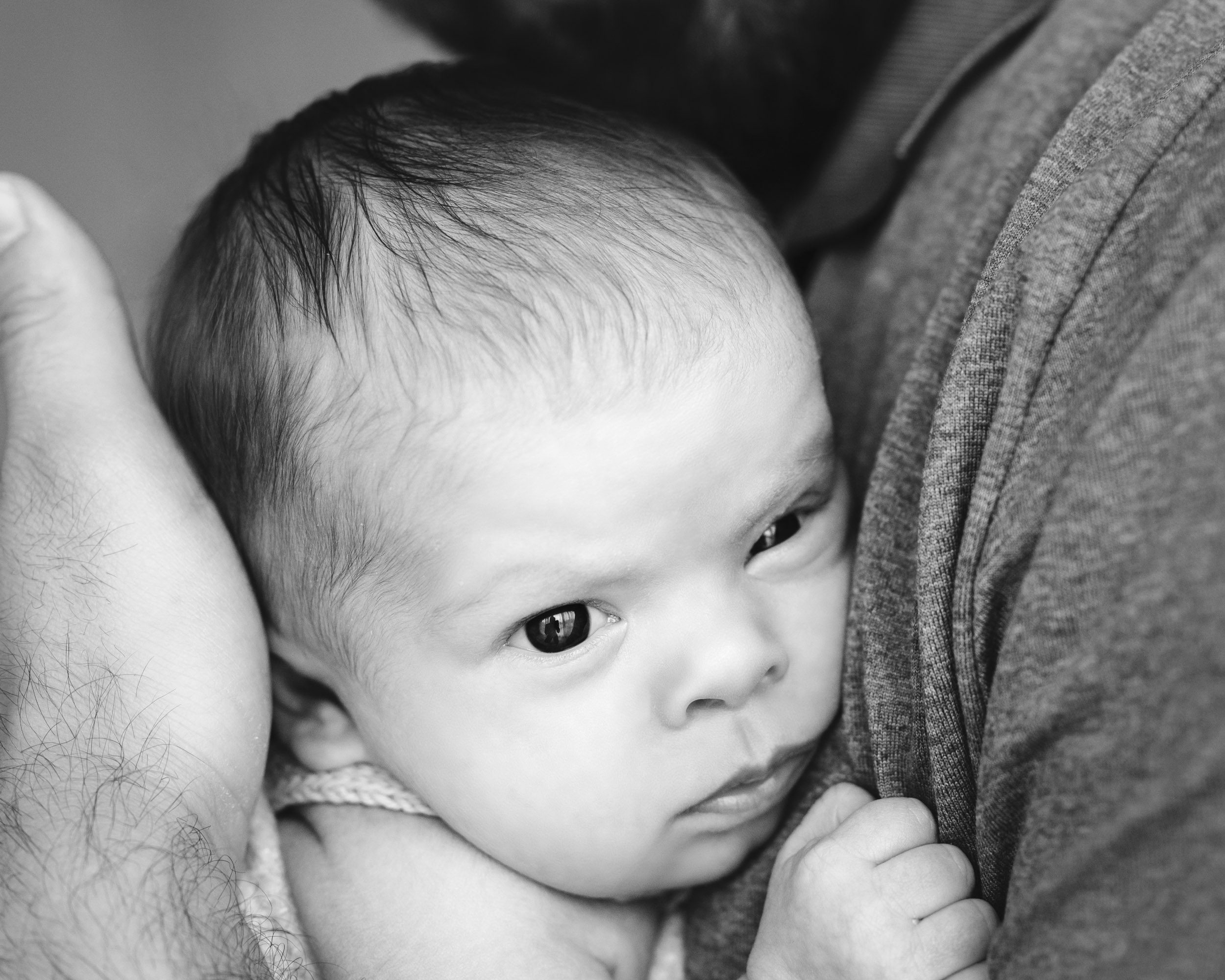 a close up black and white picture of a baby girl snuggled up against her dad's chest during a studio newborn photoshoot
