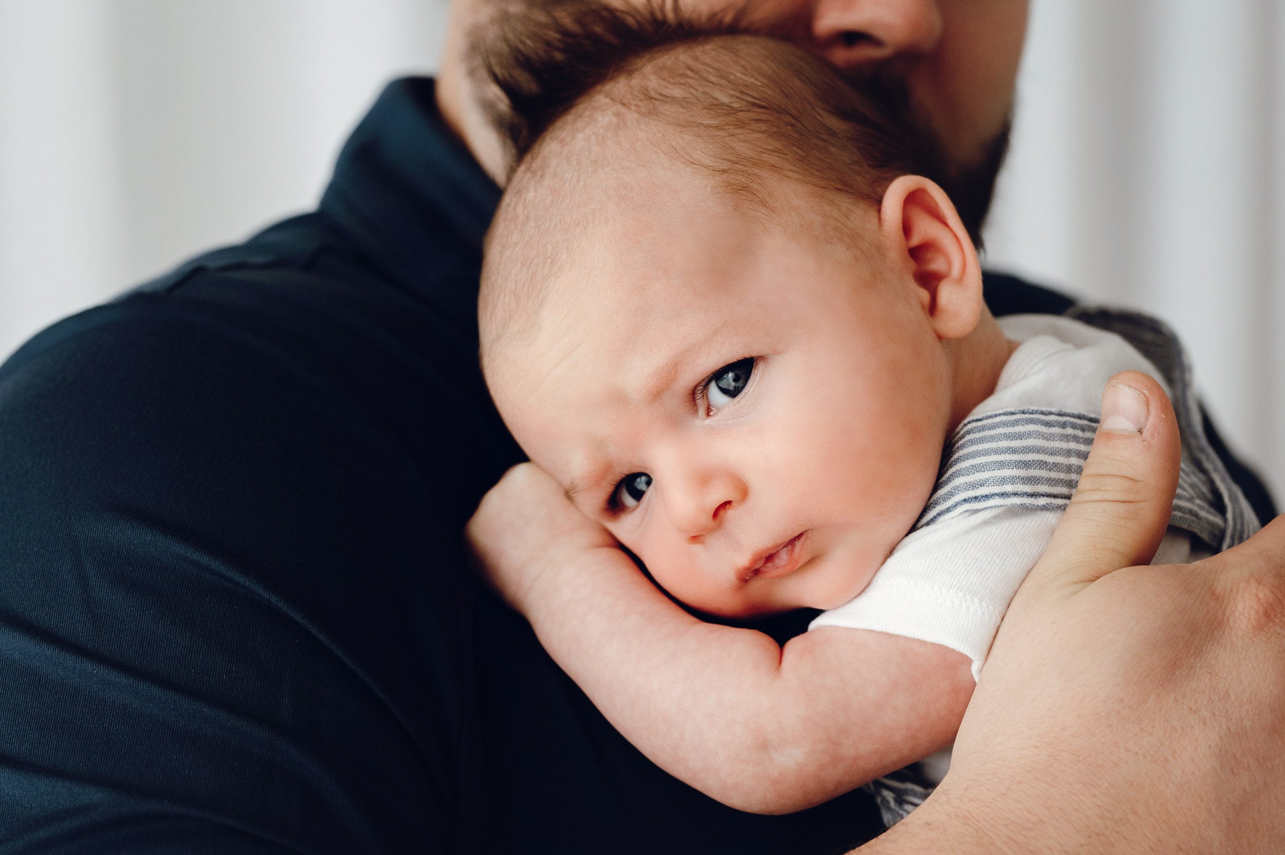 an 8 week old baby boy snuggled up against his dad's chest as the looks directly at the camera with a pouty face during a newborn photoshoot