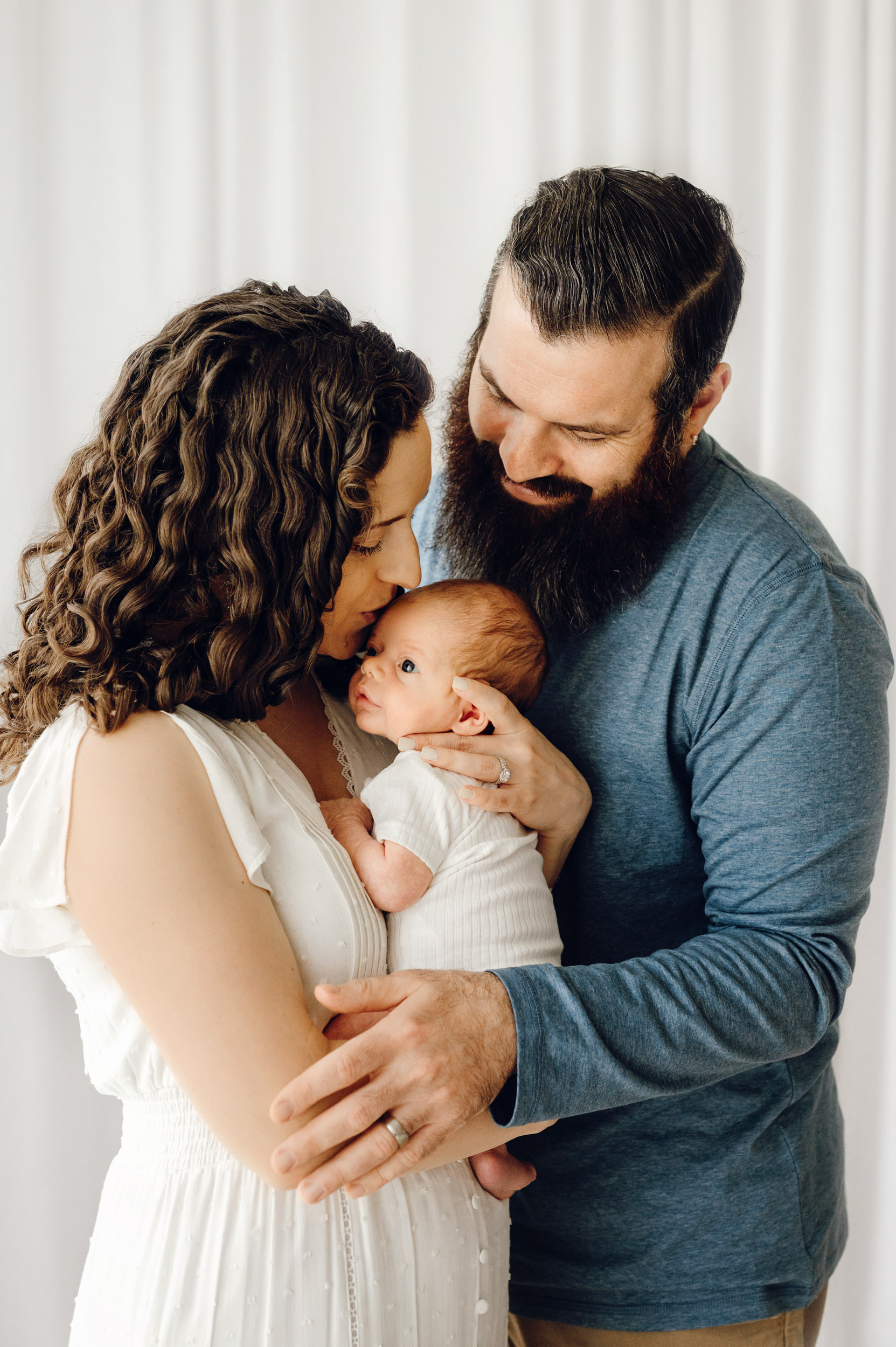 new parents holding their newborn son as dad smiles down at him and mom kisses him on the head during a Philadelphia newborn photo session