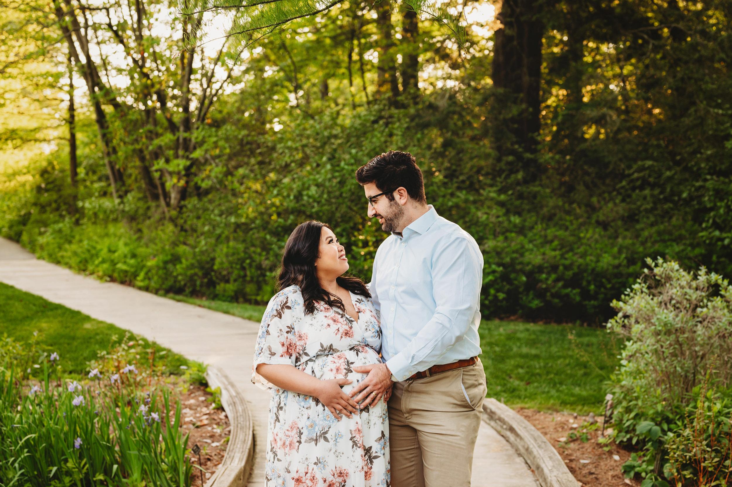 expecting parents standing on a bridge and smiling at each other as they both touch mom's belly during a Main Line maternity photography session