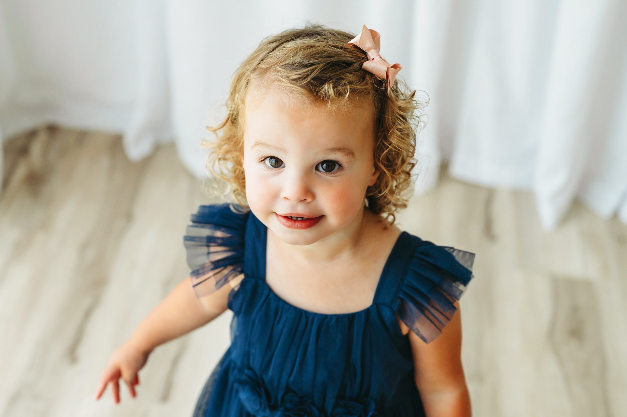 a picture taken from above of a little girl wearing a blue dress looking up at the camera above her during a toddler milestone photos session