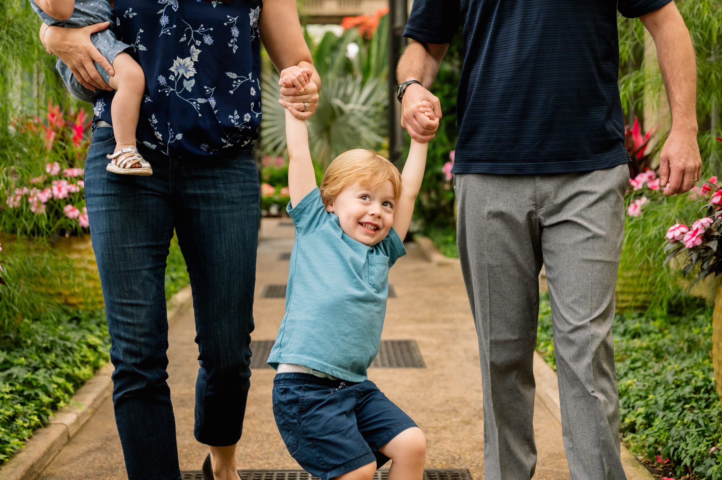 a close up picture of a young boy holding both of his parents' hands and swinging as he looks up toward the sky during a Philadelphia family photoshoot