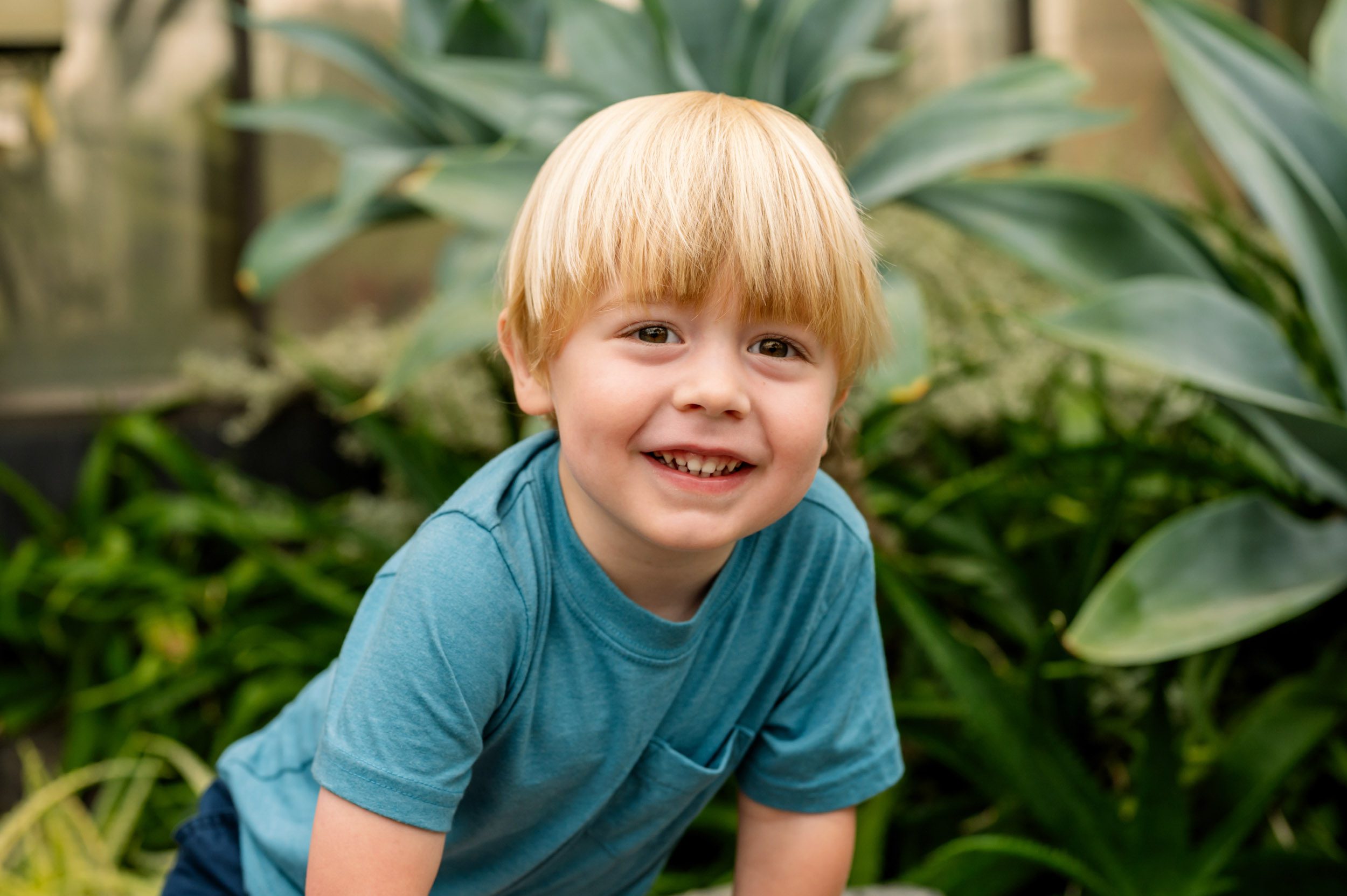 a young boy sitting in a greenhouse and smiling directly at the camera during a Philadelphia family photoshoot