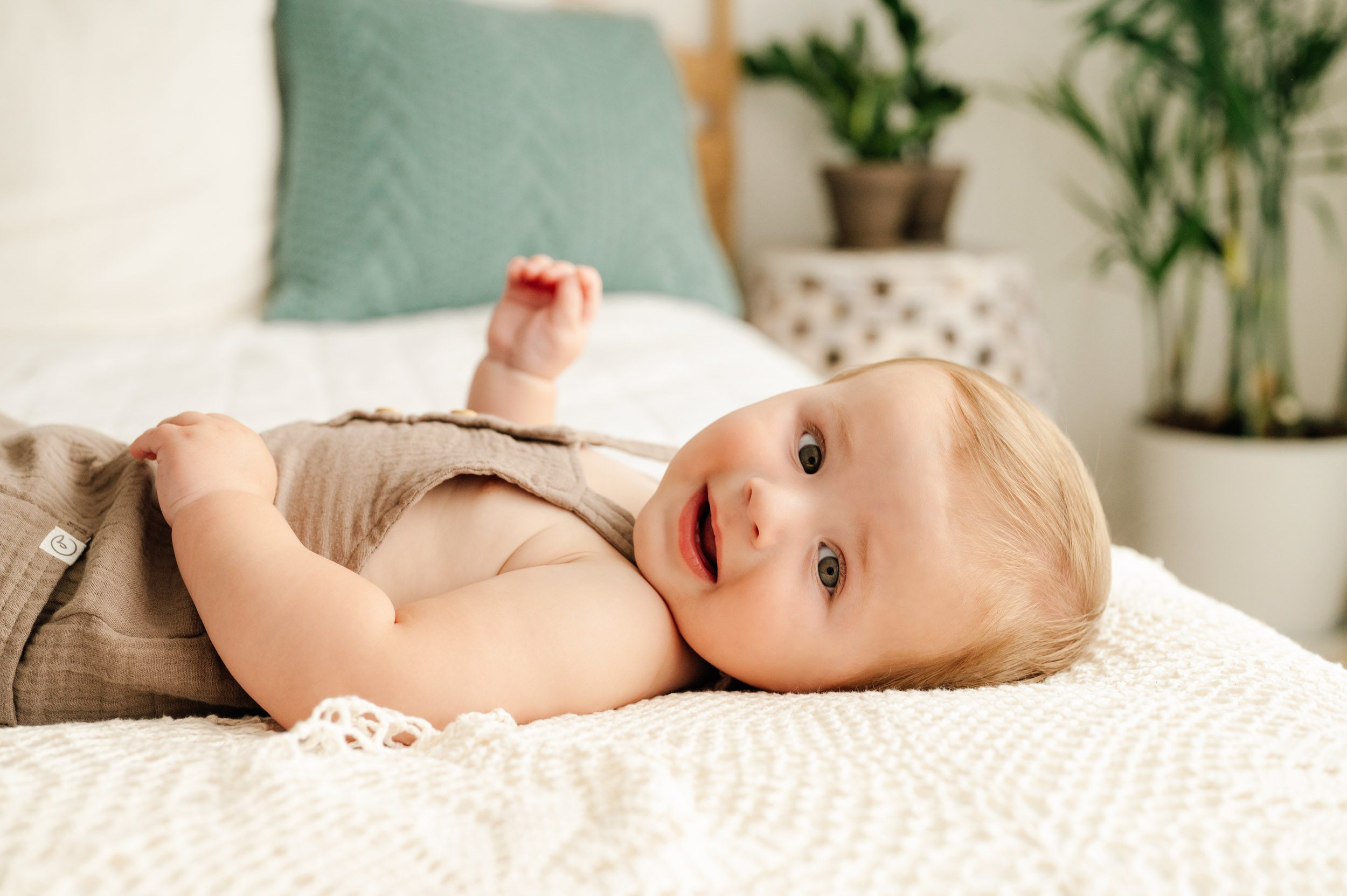 a baby boy laying on a bed with his head turned to the side as he looks directly at the camera during an 8 month baby milestone session