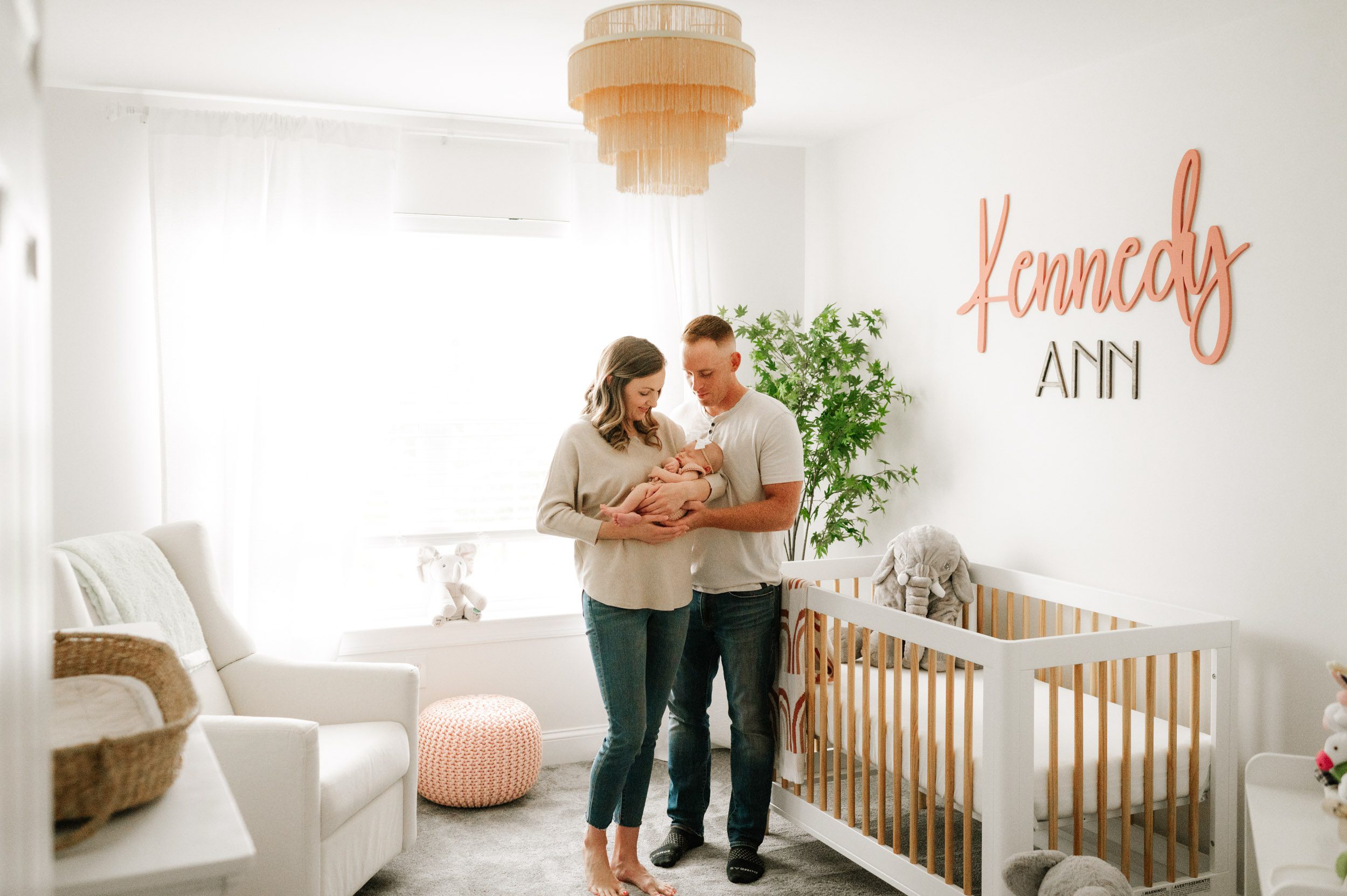 new parents standing in their baby's nursery smiling down at their daughter cradled in mom's arms during an in home newborn photography session