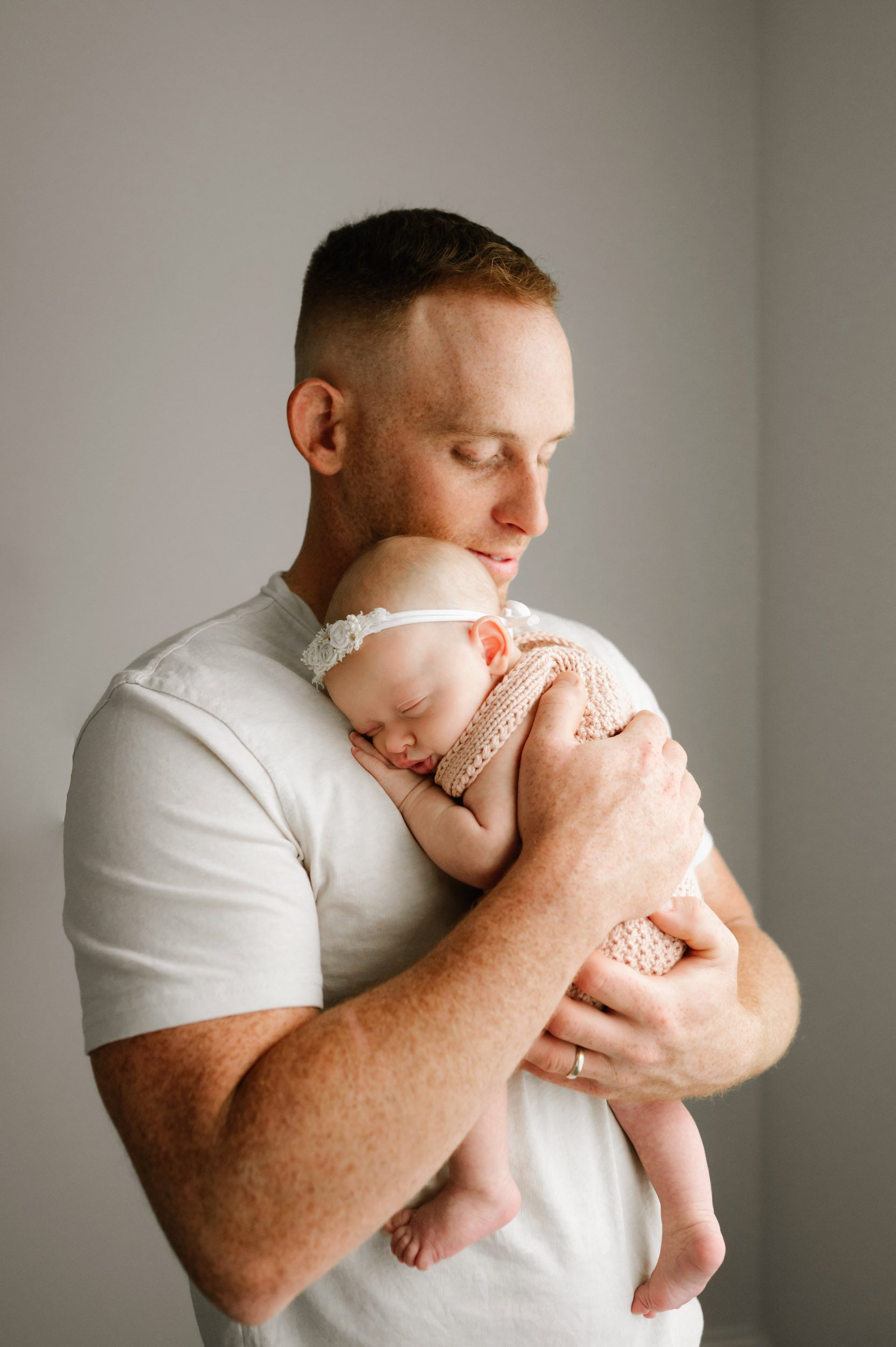 a baby girl snuggled up against her dad's chest and sleeping peacefully during an in home newborn photography session