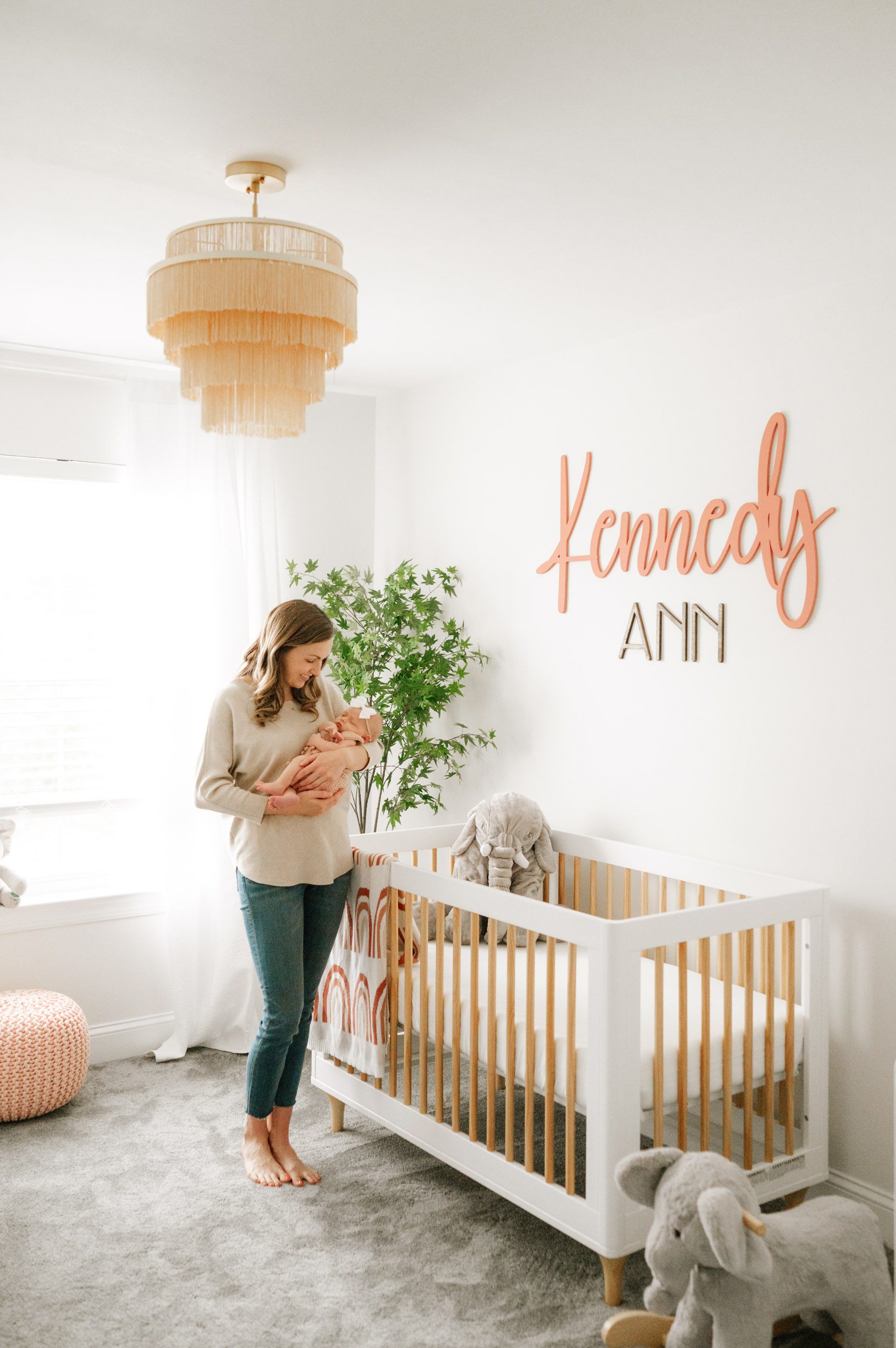 a new mom standing in her baby's nursery in front of the crib as she cradles her baby girl in her arms and smiles down at her during an in home newborn photography session