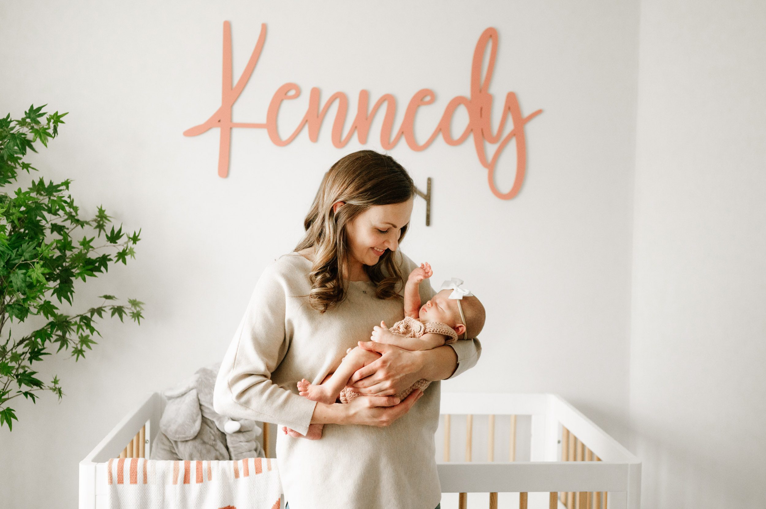 a new mother standing in front of her baby's crib and cradling her baby girl in her arms as she smiles down at her during an in home newborn photography session