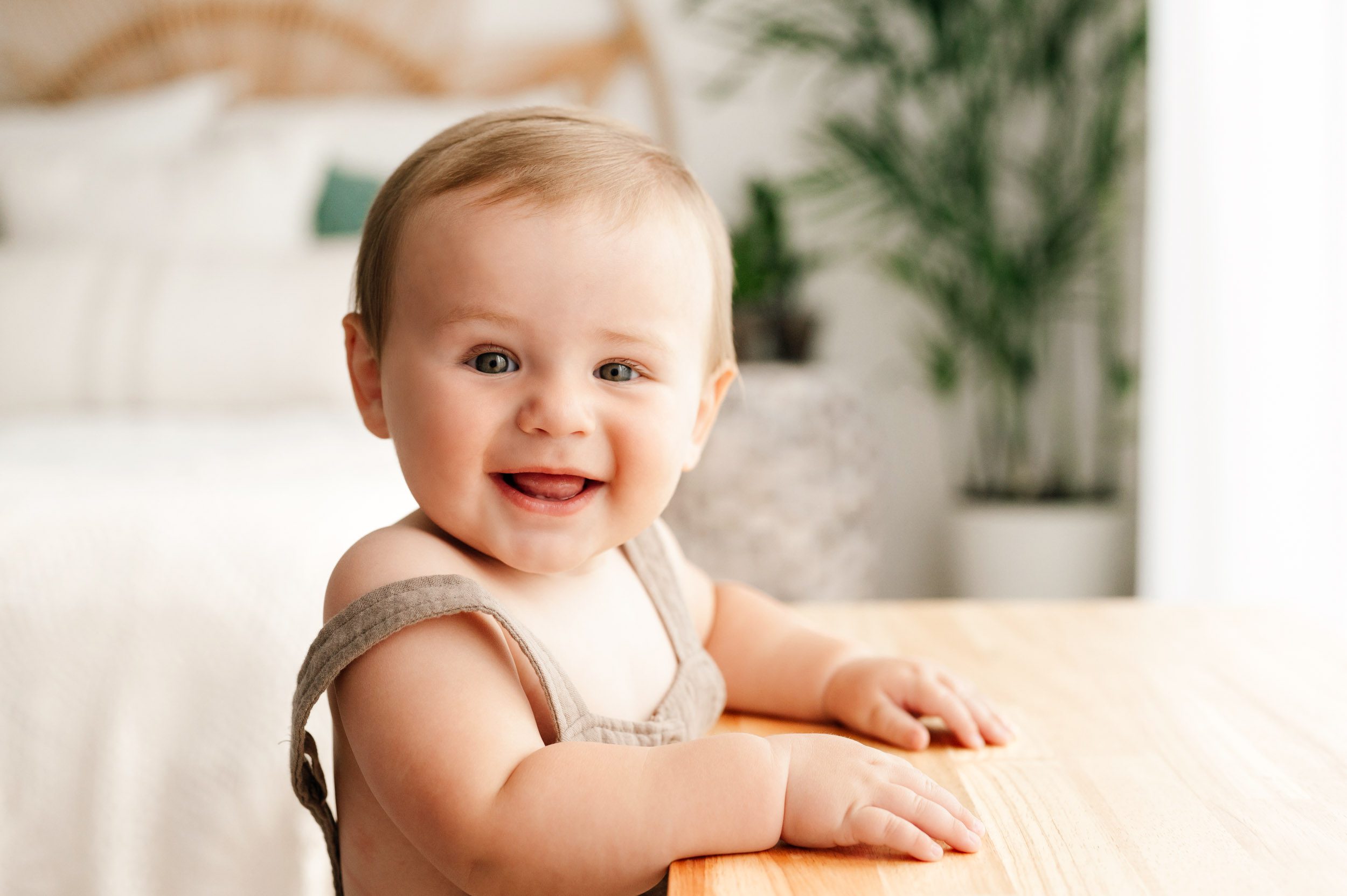 a baby boy holding onto a bench and smiling at the camera during a baby milestone photoshoot