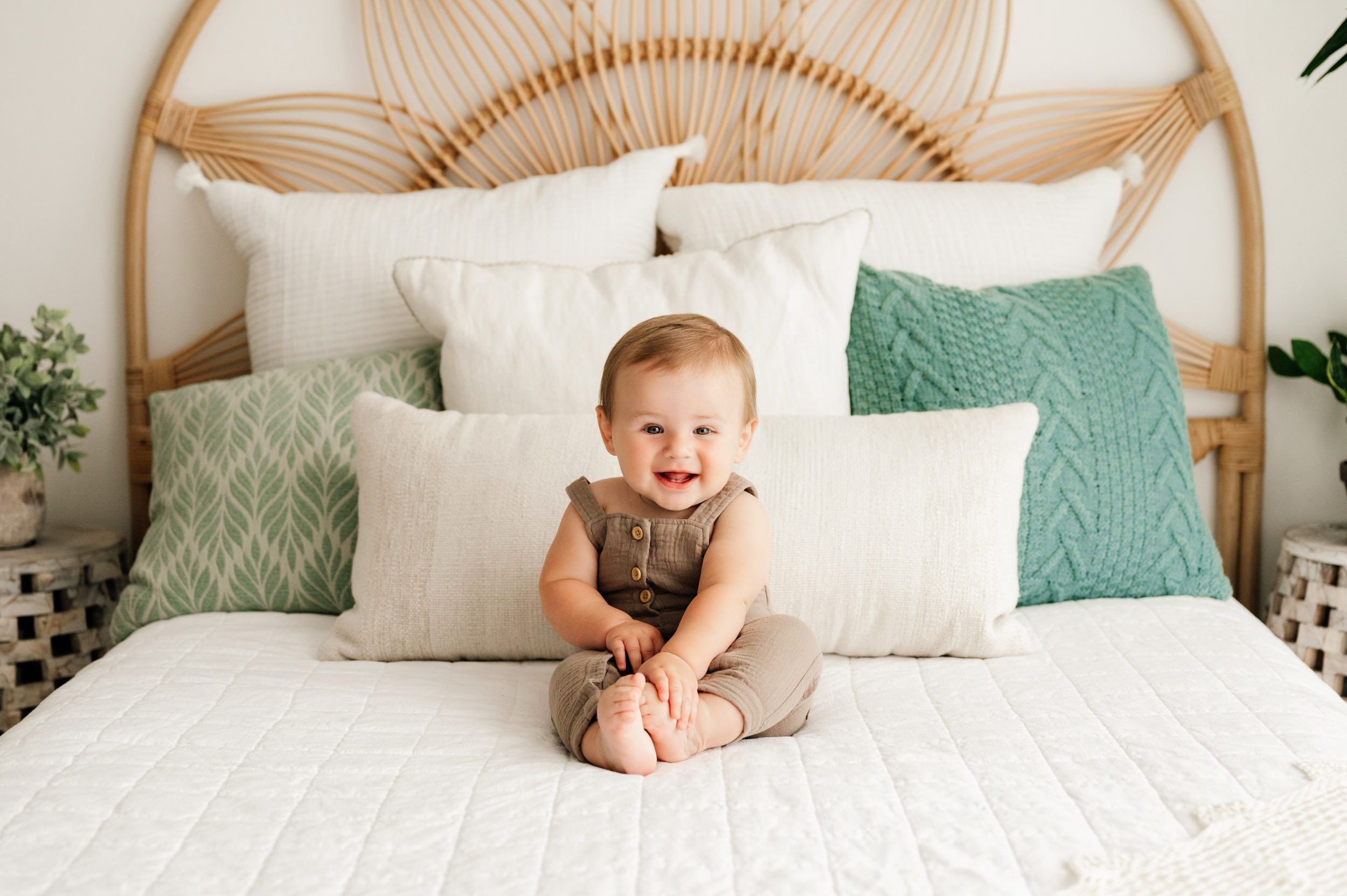 a baby boy sitting on a bed and grabbing his toes as he smiles at the camera during an 8 month milestone photoshoot