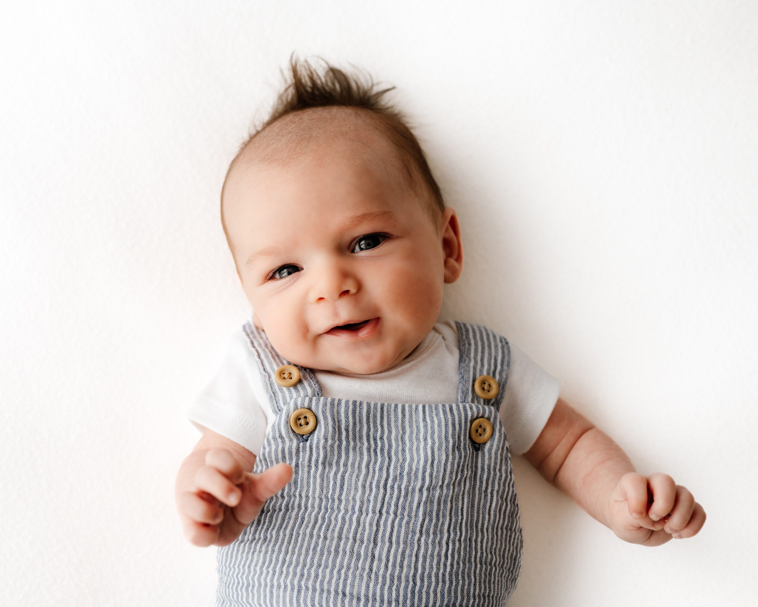 a baby boy wearing a blue and white striped romper laying on a white backdrop during a newborn photo session