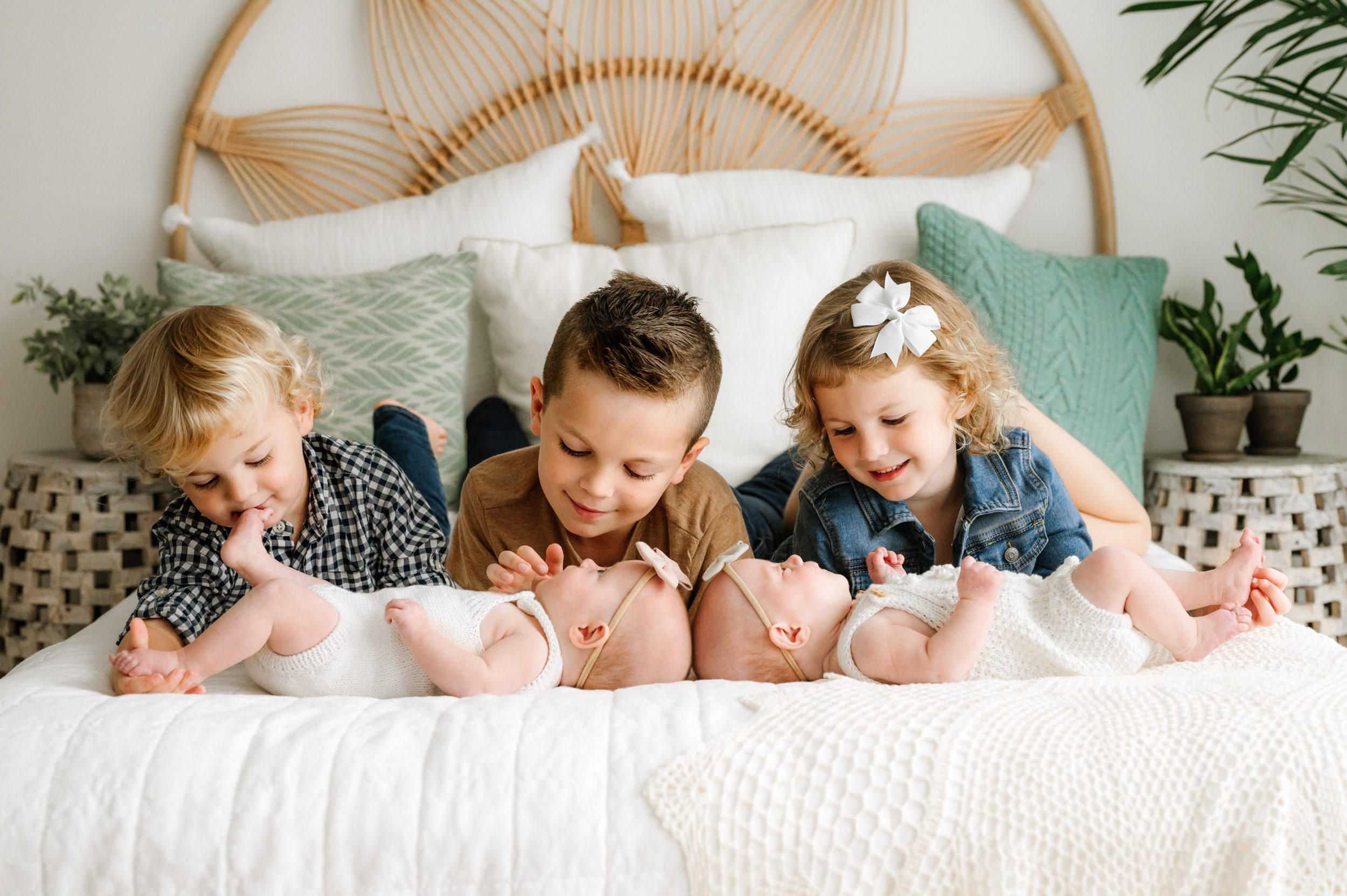 twin baby girls laying on a bed while their two older brothers and older sister lay behind them and smile down at them and give them kisses during a newborn photoshoot