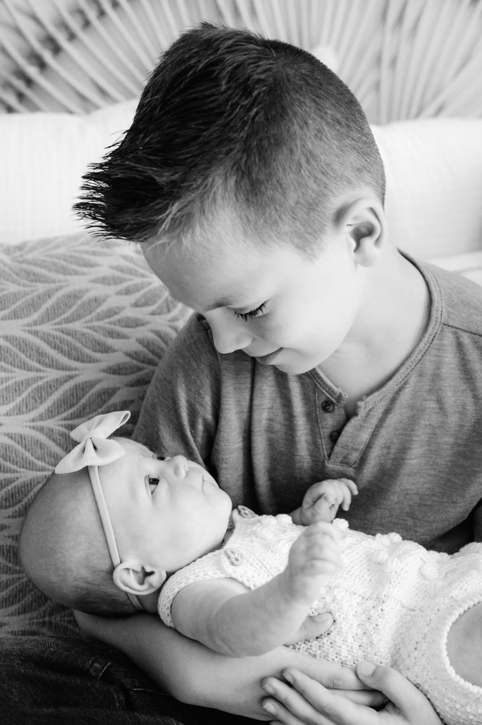 a black and white picture of a big brother holding his baby sister in is arms and smiling down at her during a newborn photoshoot