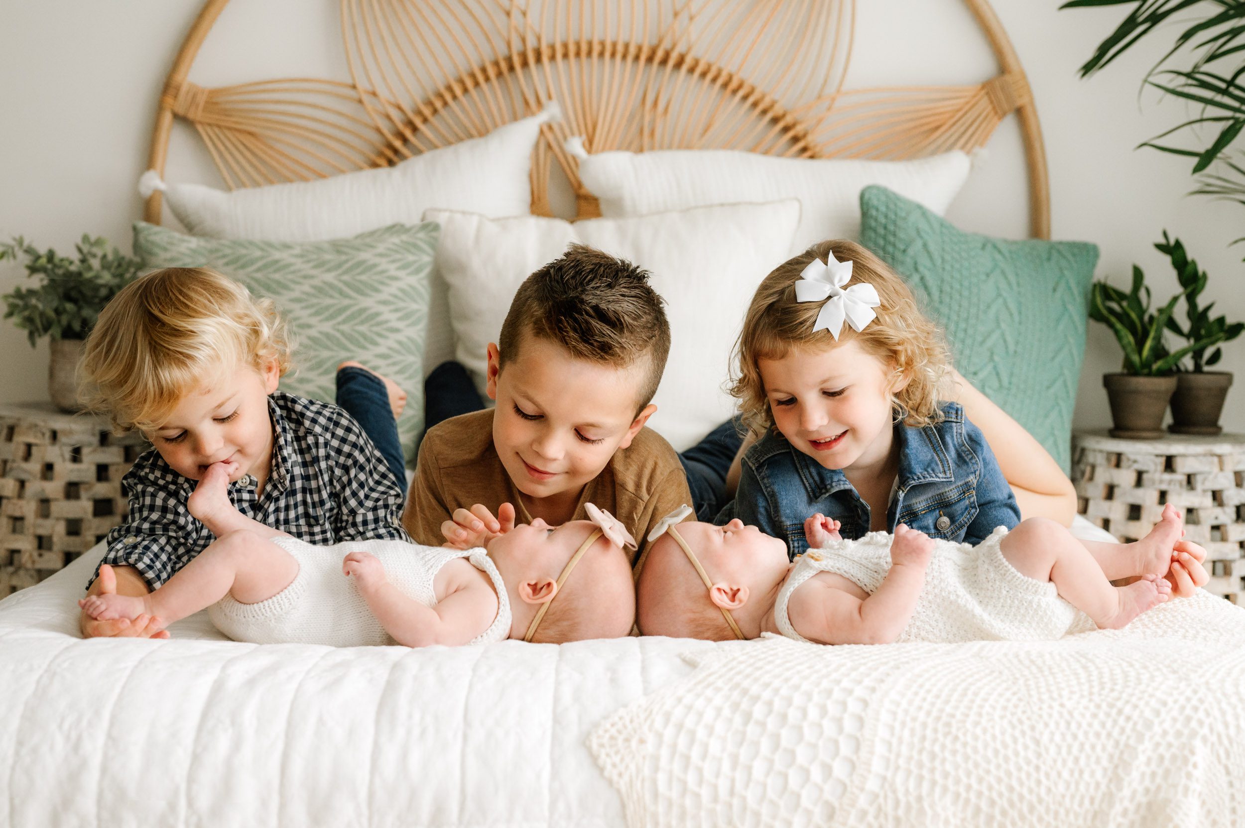 twin baby girls laying on a bed with their two older brothers and older sister laying behind them and smiling down at them during a lifestyle newborn photos session