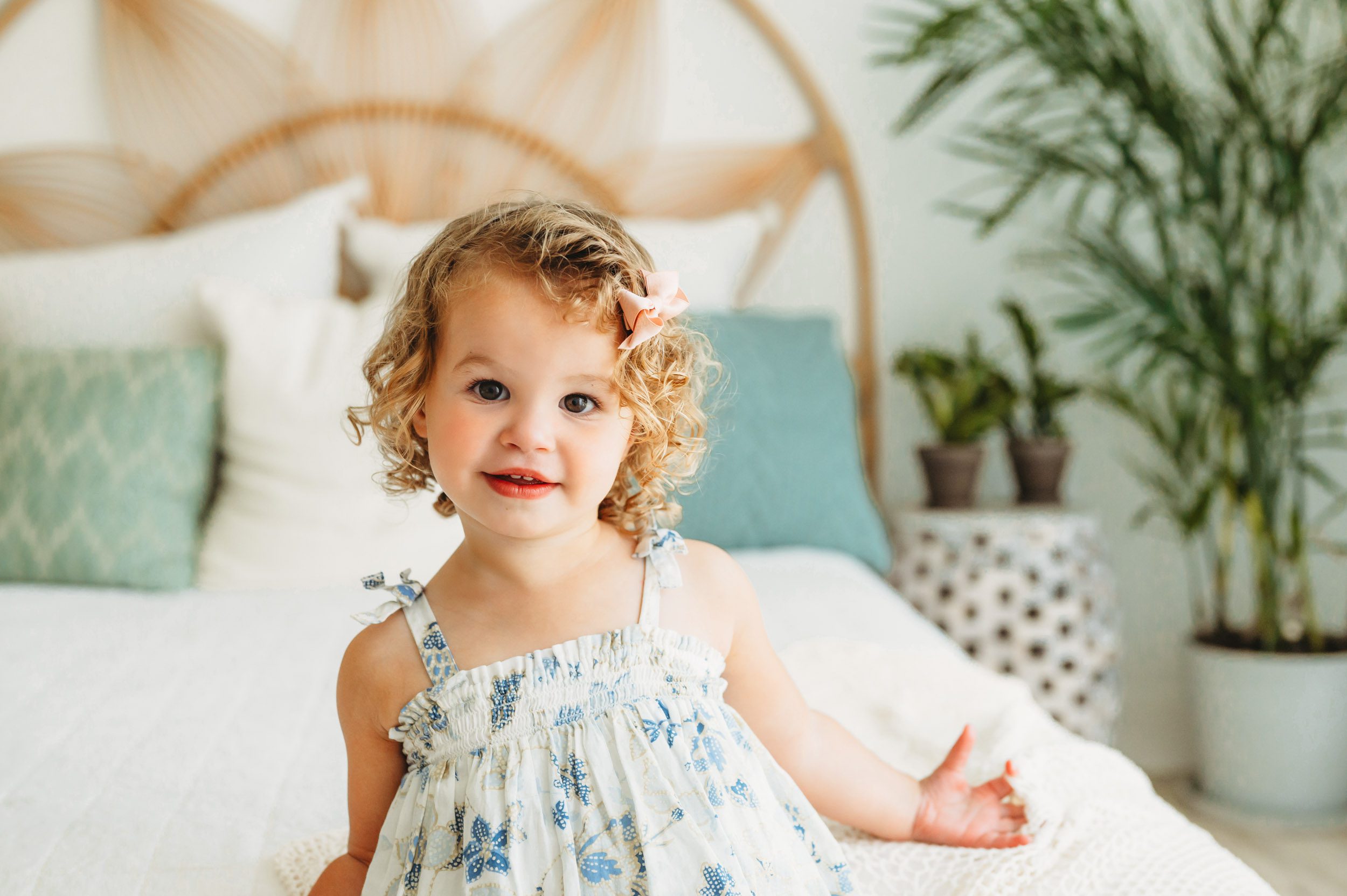 a young girl standing in front of a bed and smiling at the camera during a 2nd birthday toddler milestone photoshoot