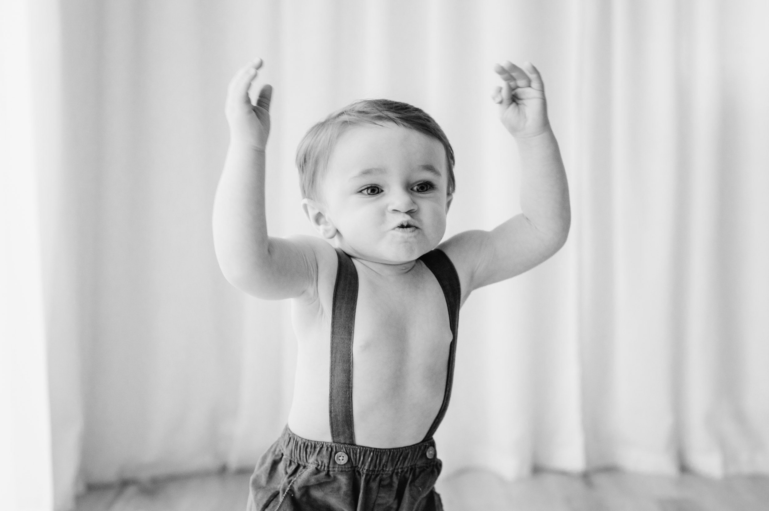 a black and white picture of a young boy raising his hands up in the air and running with his lips pursed in determination during a Pottstown toddler milestone photography session