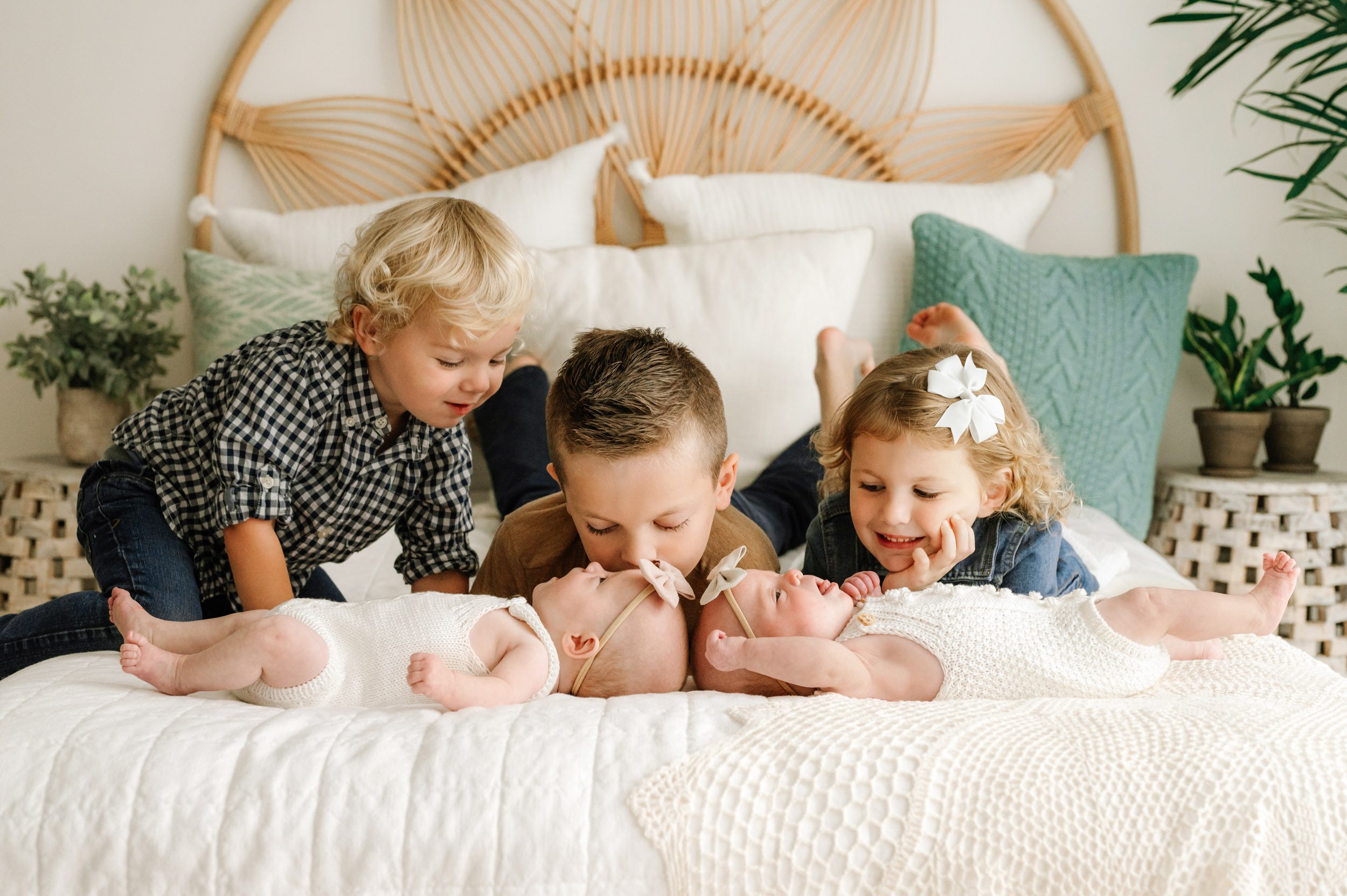 twin baby girls laying on a bed with their two older brothers and older sister laying behind them and smiling down at them during a lifestyle newborn photoshoot
