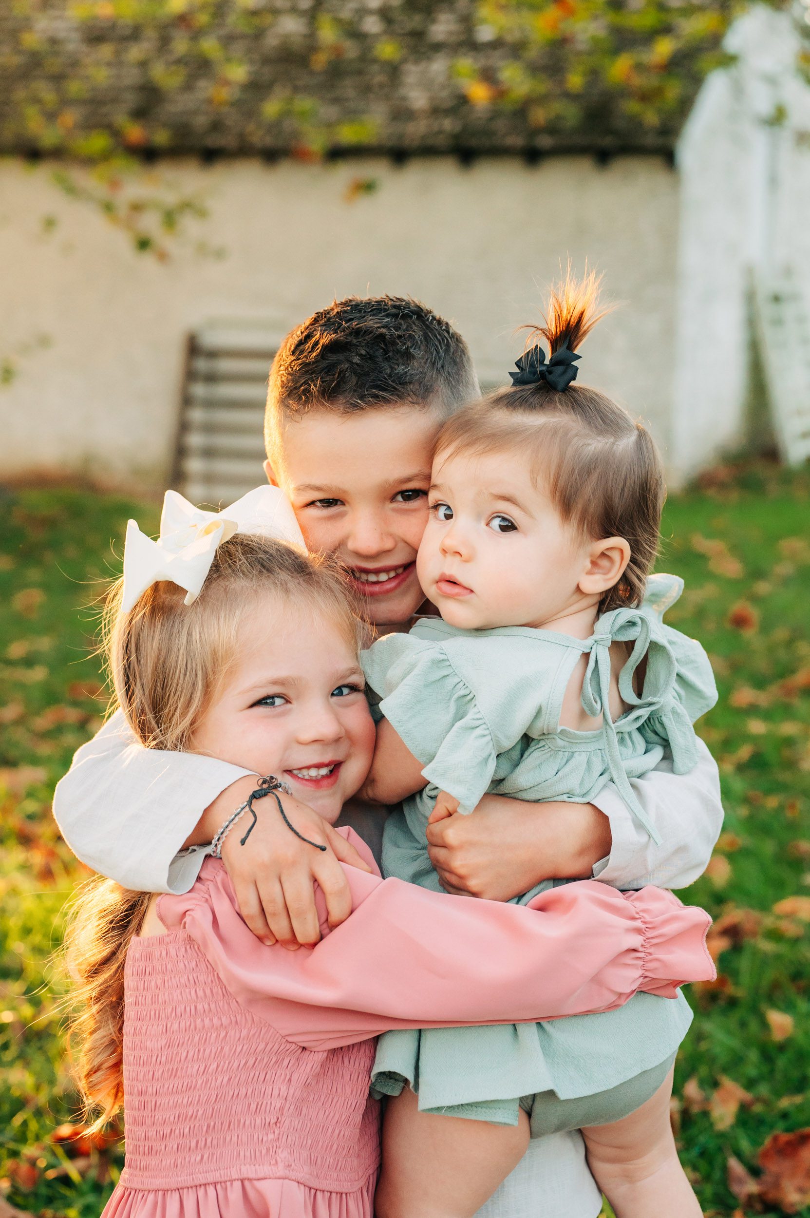 a close up picture of three young siblings hugging each other and smiling right at the camera during a family photography session