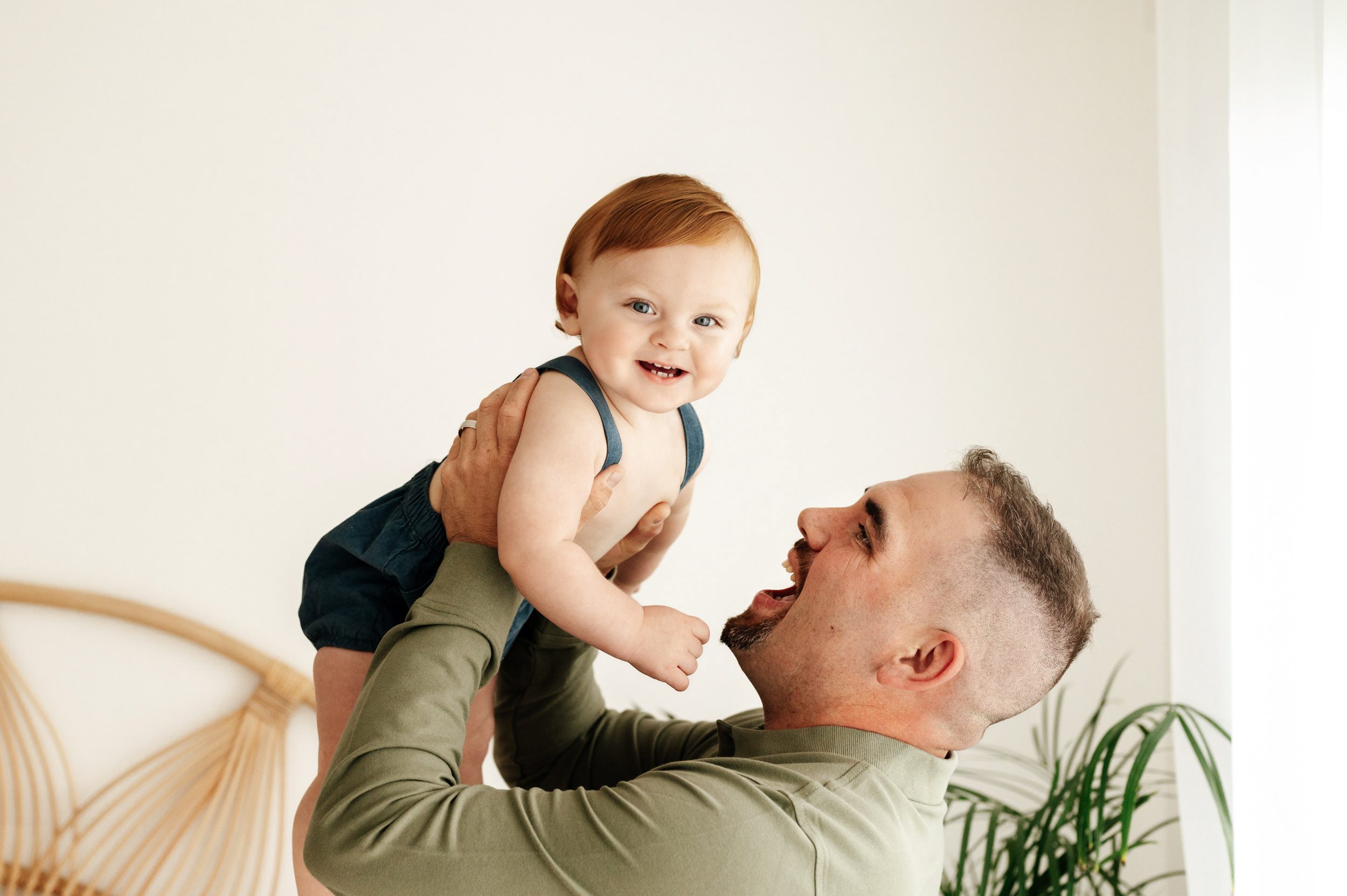 a father lifting his young son up in the air while the boy looks at the camera and smiles