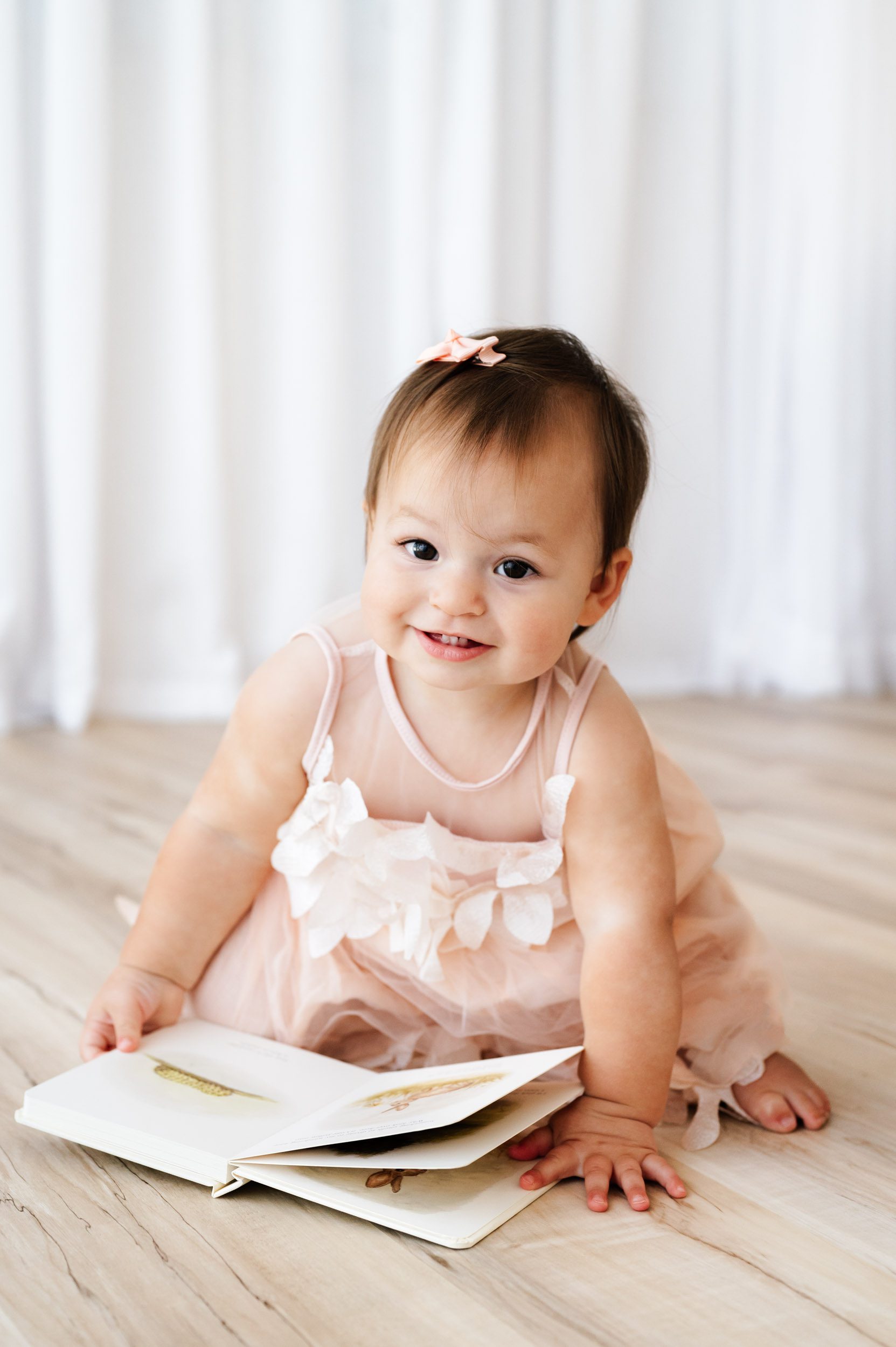 a young girl wearing a pink dress crouching down to look at a book during a Pottstown baby milestone photography session