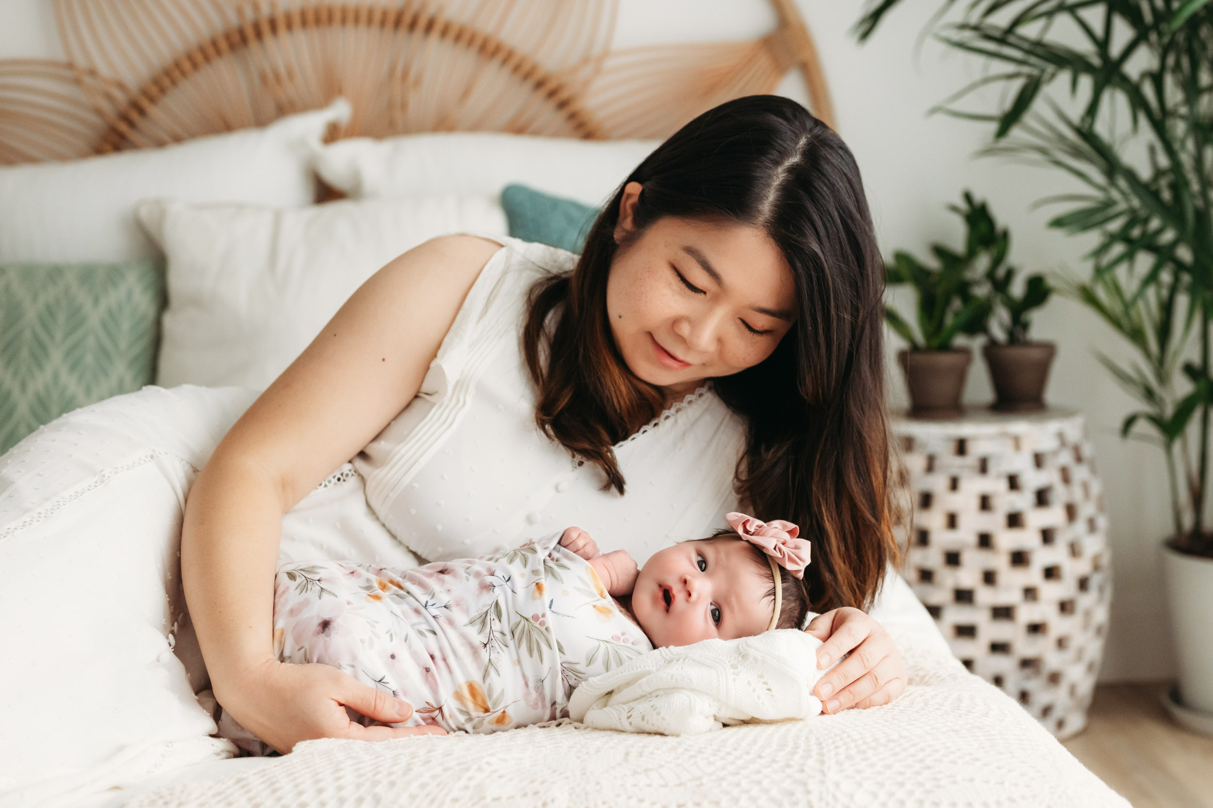 a new mom laying on a bed with her baby girl and smiling down at her during a lifestyle newborn photoshoot