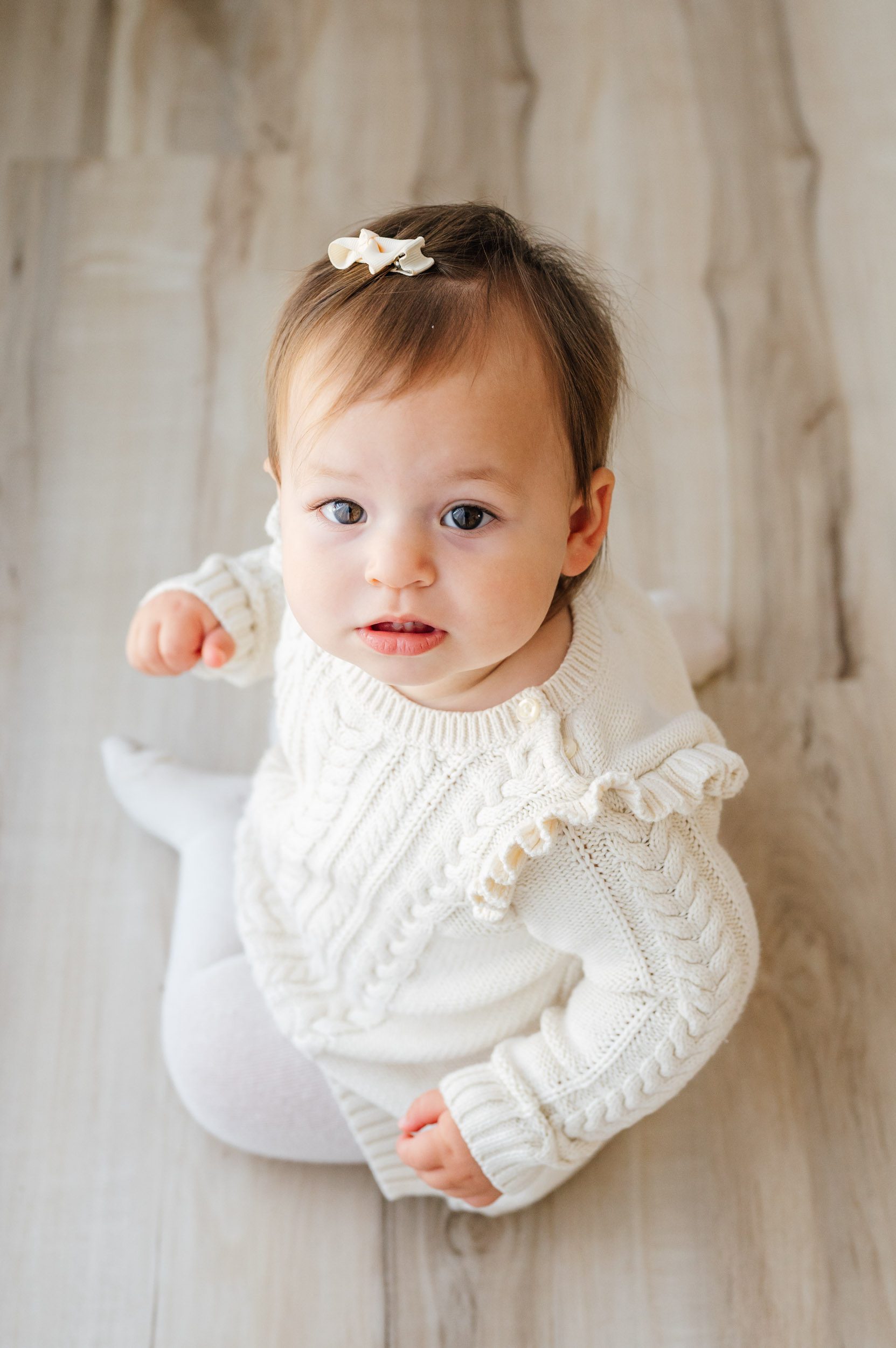 a picture taken from above of a little girl wearing an ivory cable knit dress looking up and gazing directly into the camera during a Pottstown baby photography session