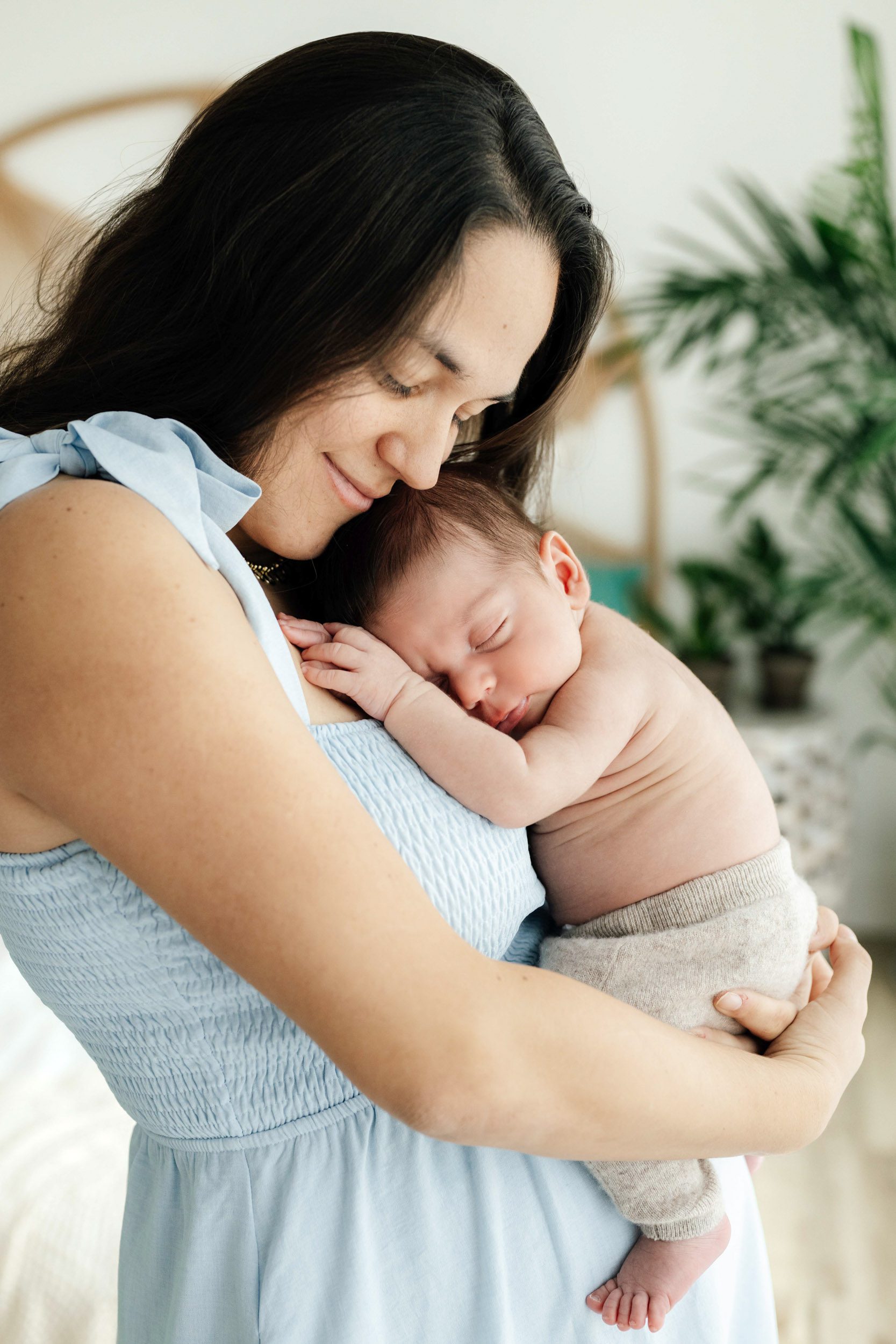 a baby boy sleeping peacefully snuggled up against his mom's chest as she smiles down at him during a newborn photoshoot