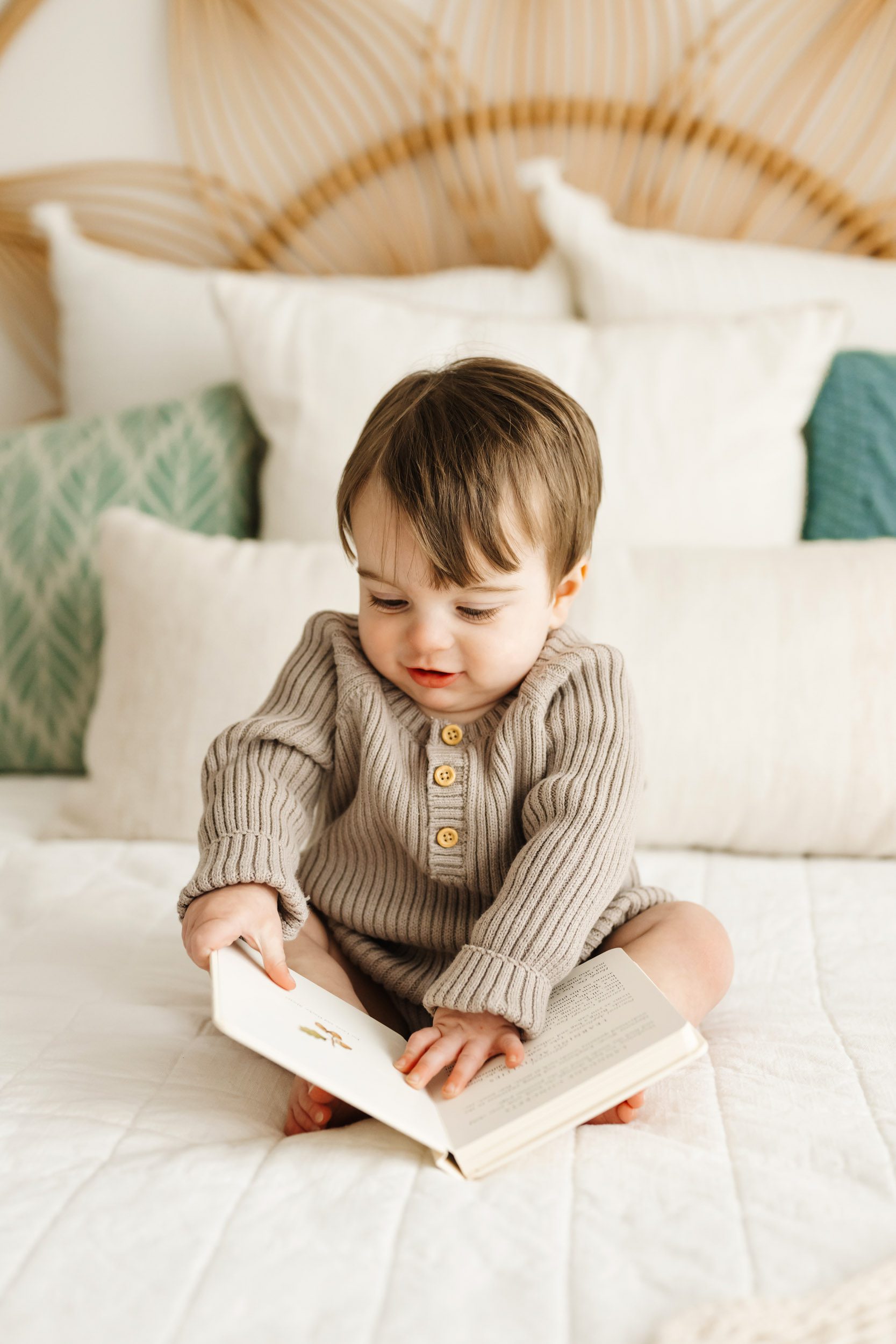 a young boy sitting on a bed and looking at a picture book during a 1st birthday photoshoot