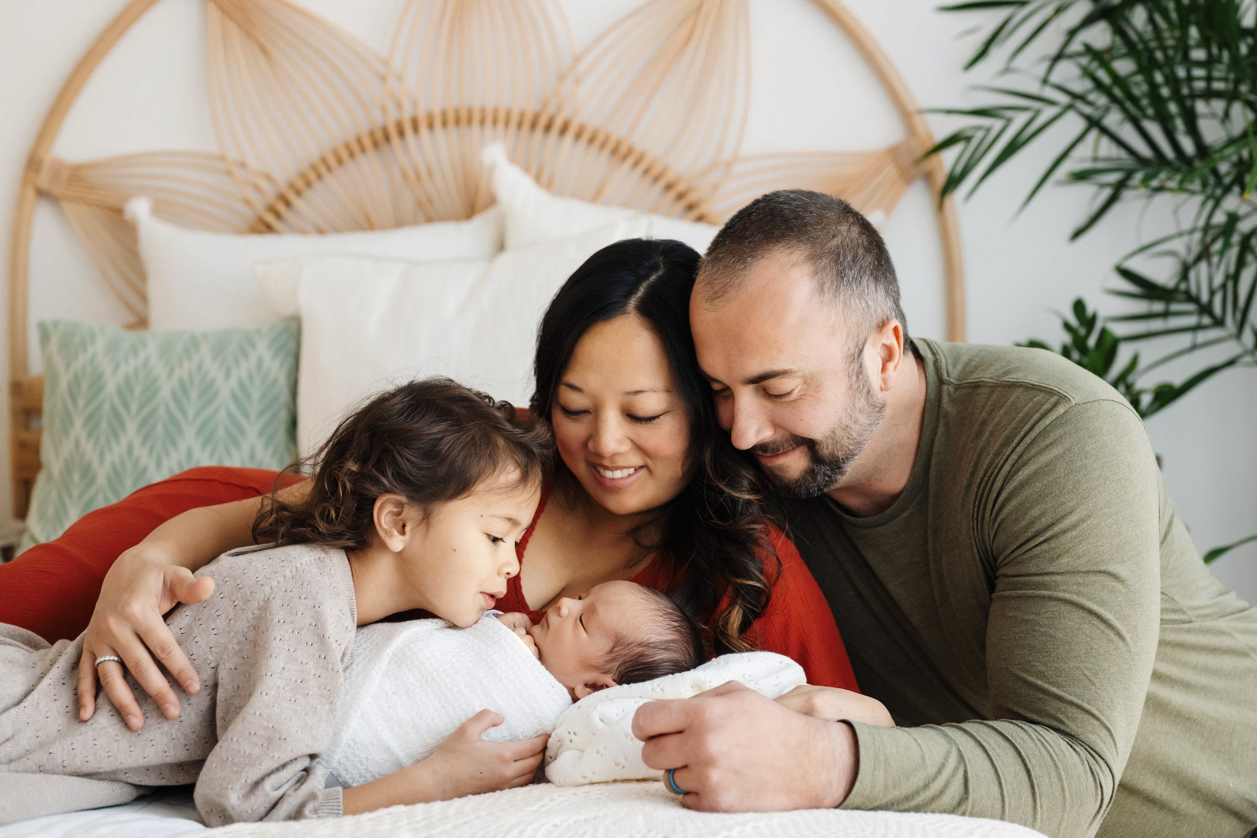 a family of four laying on a bed snuggling with their new baby boy during a family centered newborn photoshoot