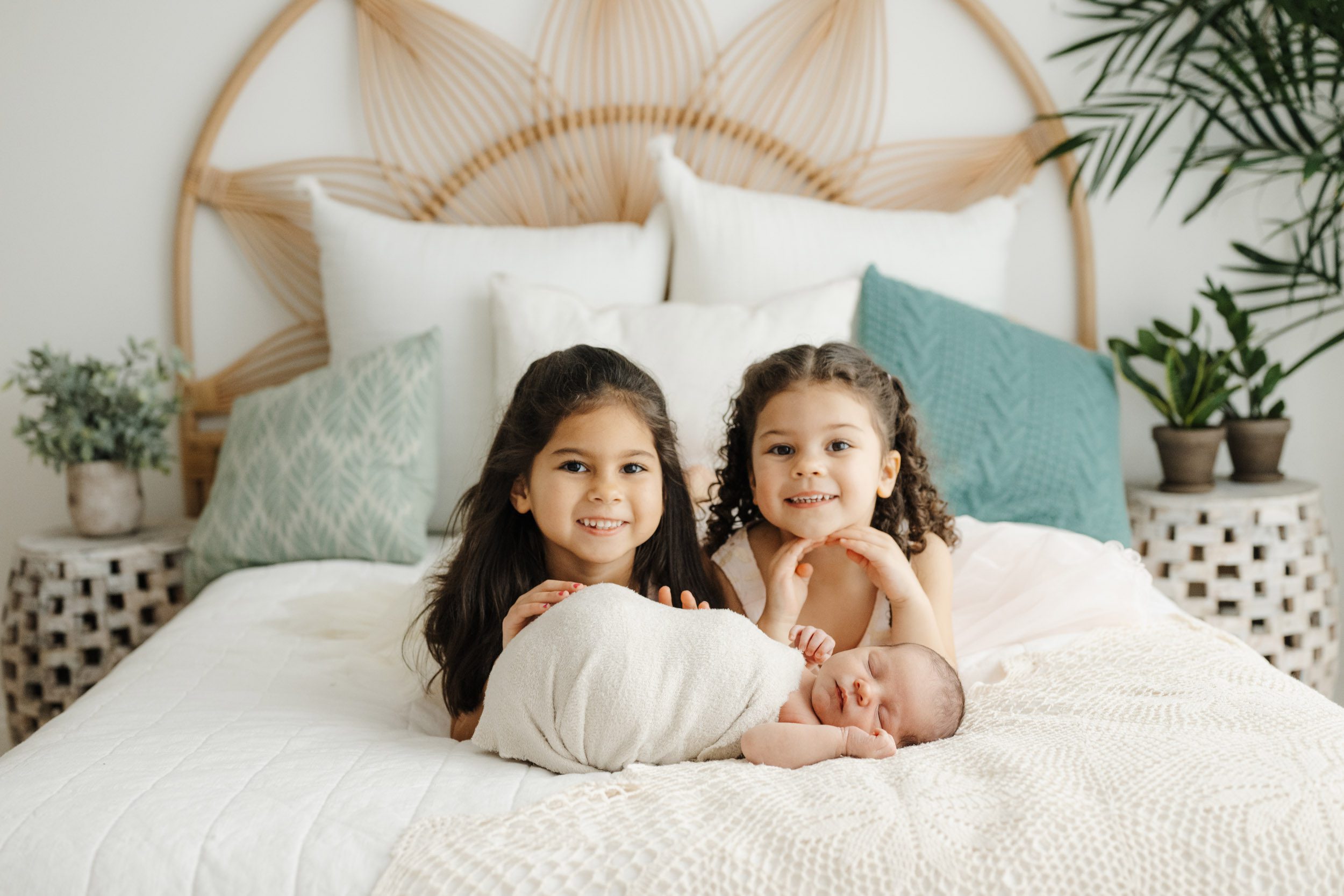 two young siblings laying on a bed with their baby brother as they both smile at the camera during a newborn photos session