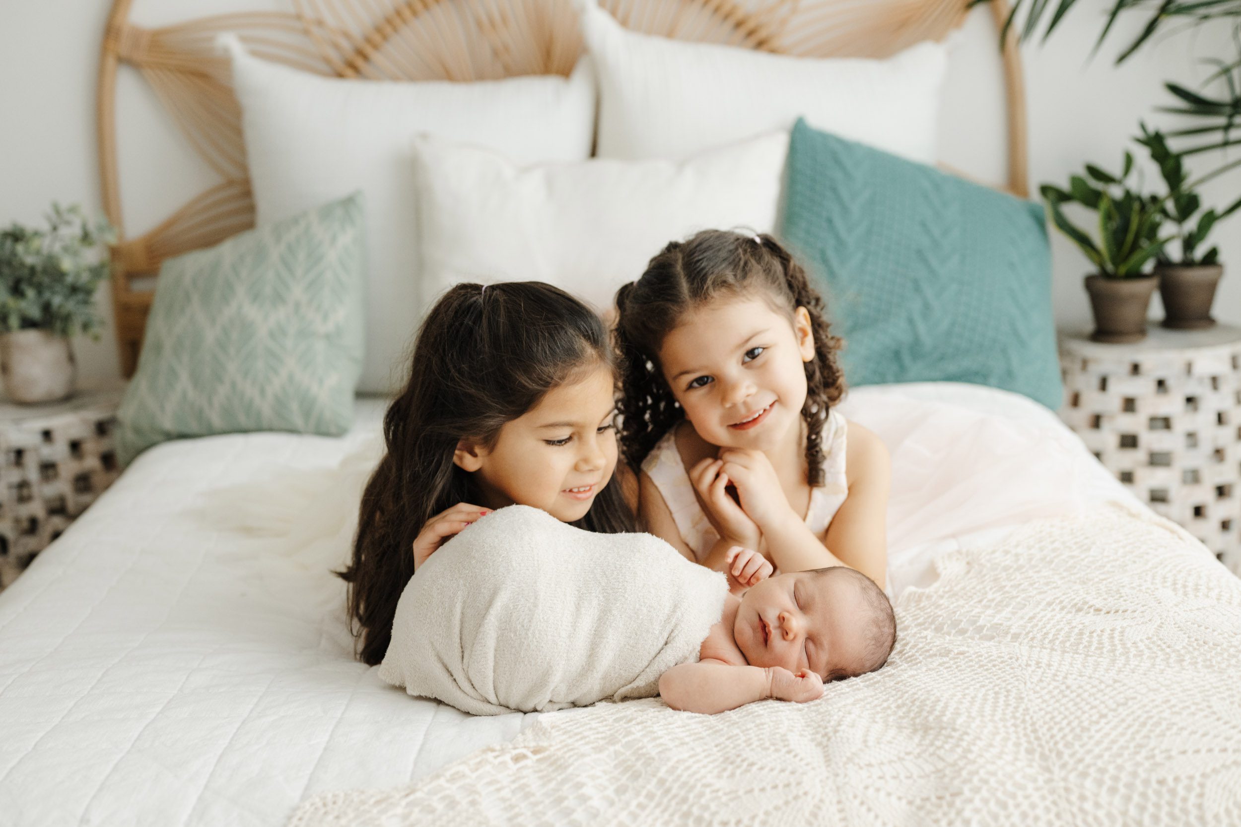 a baby boy laying on a bed with his two young siblings laying behind him during a newborn photos session