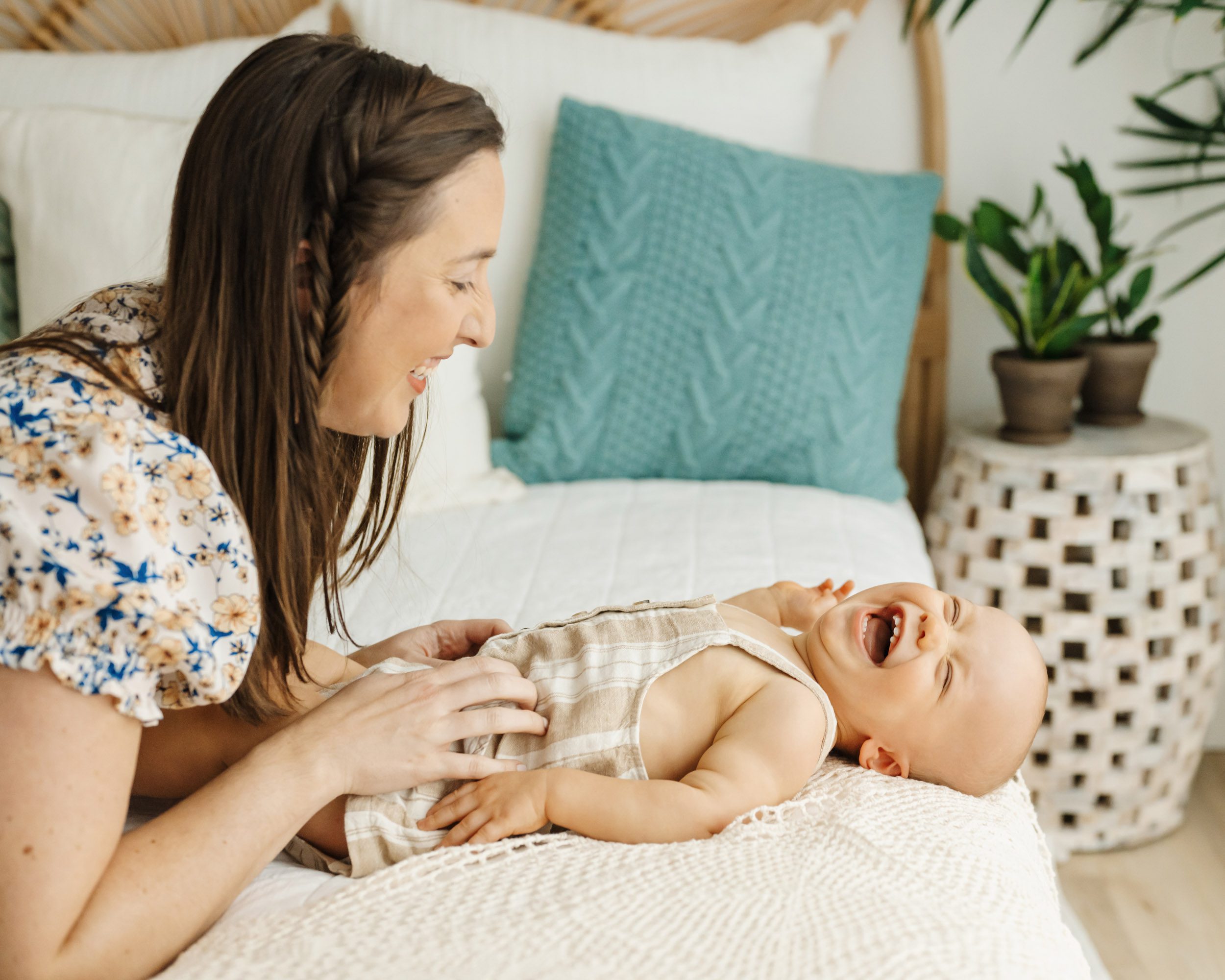 a young boy laying on a bed and laughing while his mom tickles him during a baby's 1st year photoshoot