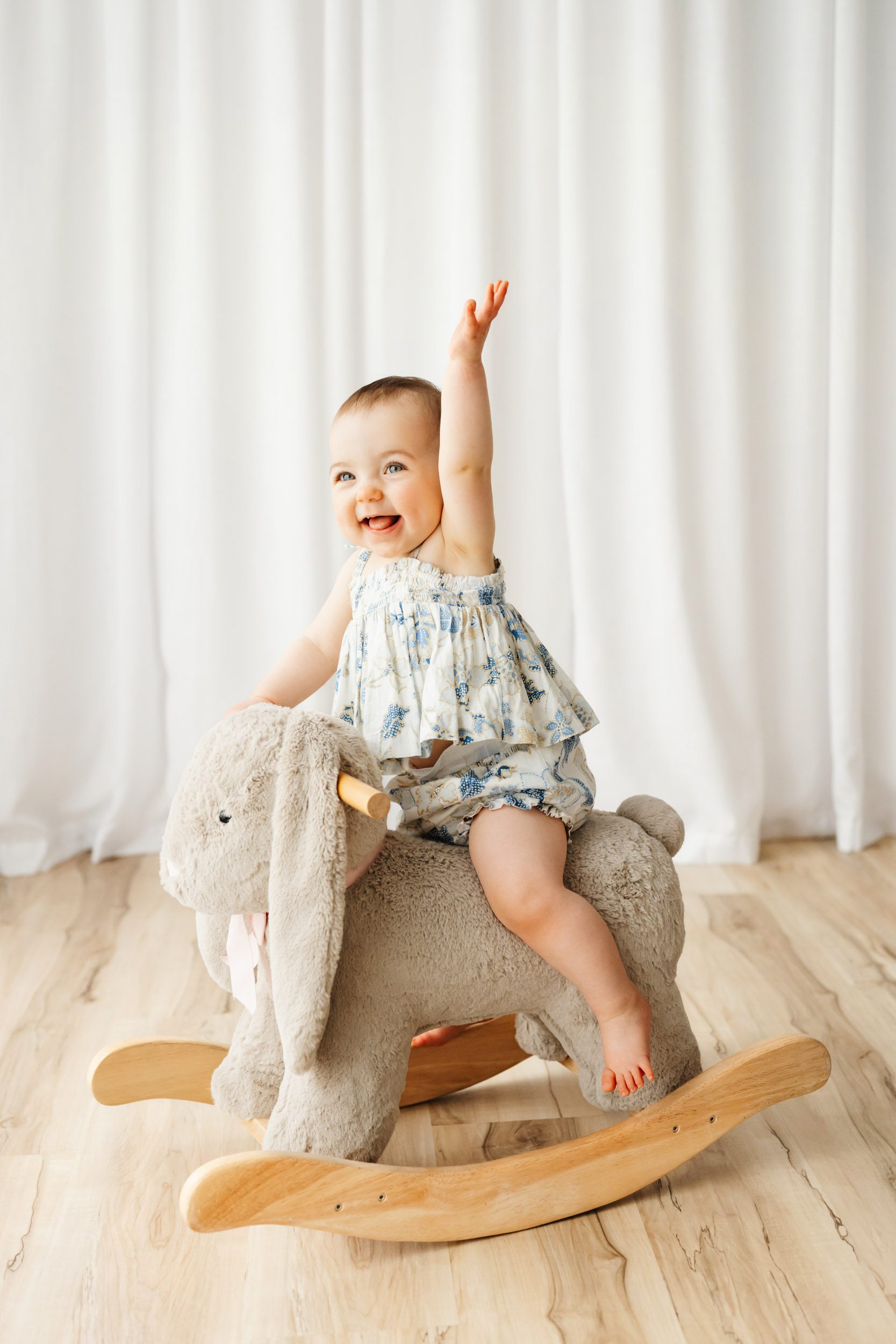 a little girl riding a toy bunny rocker and lifting her hair high up the air as she sticks out her tongue and laughs during a Pottstown 1st birthday photoshoot