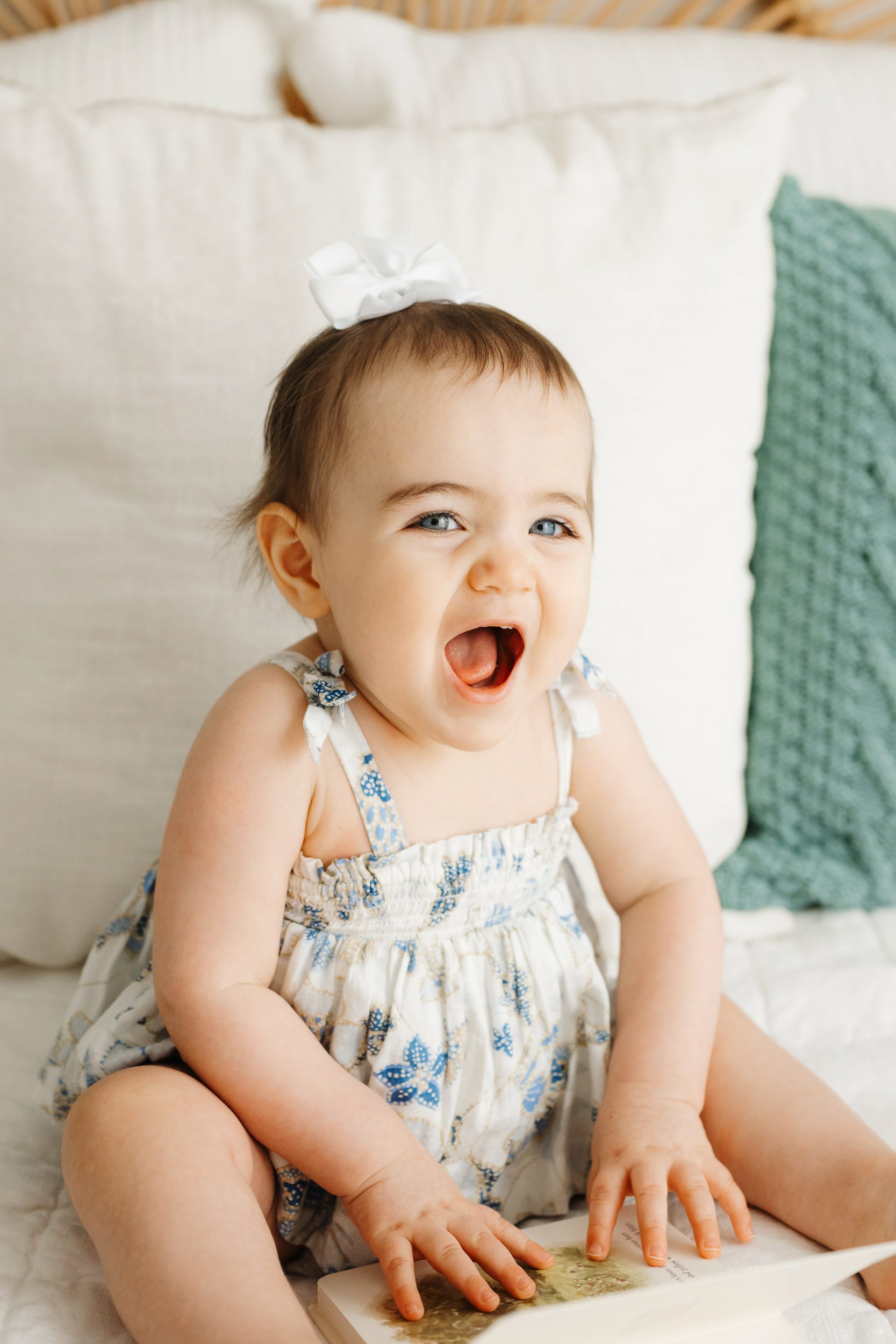 a little girl sitting on a bed and looking directly at the camera with a huge smile on her face during a 1st birthday photos session