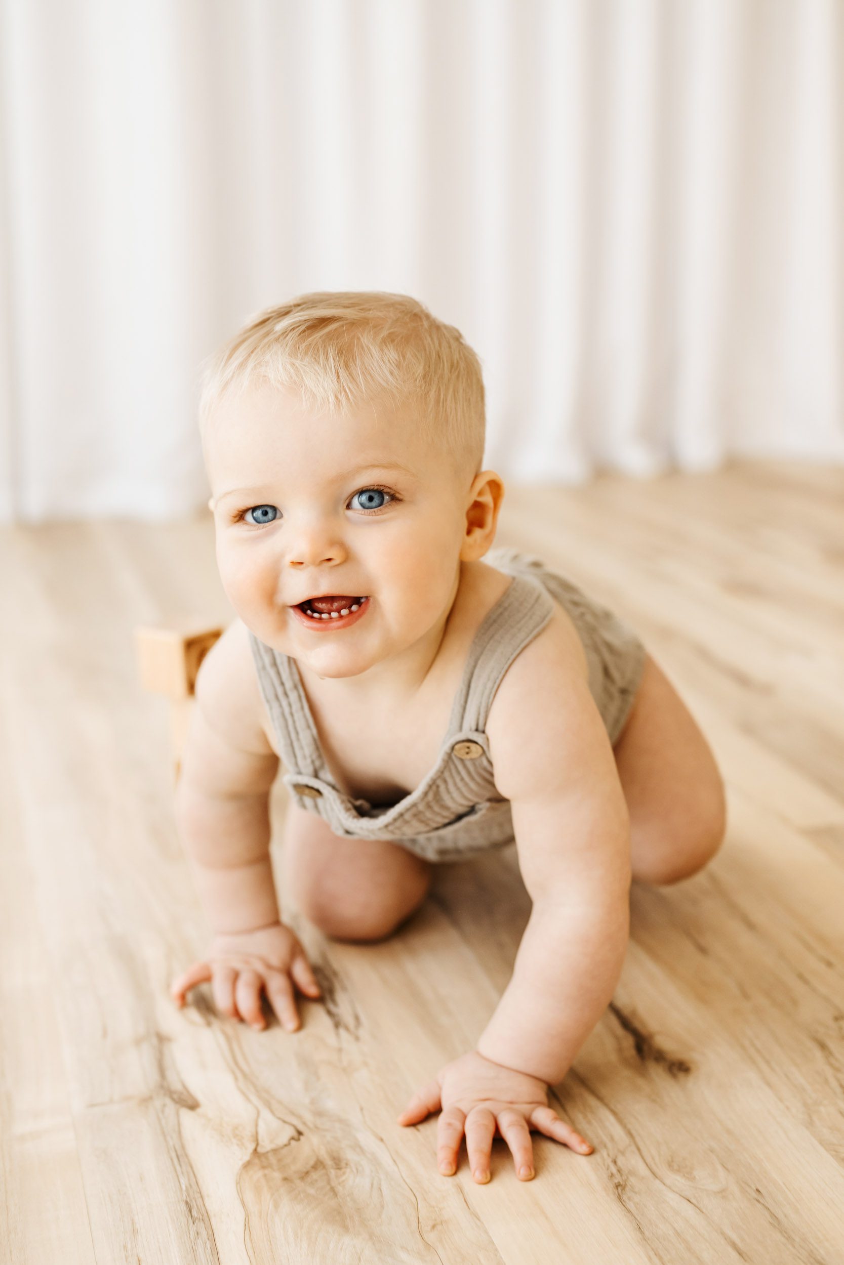 a young boy crawling across the floor and smiling at the camera during a first birthday photography session