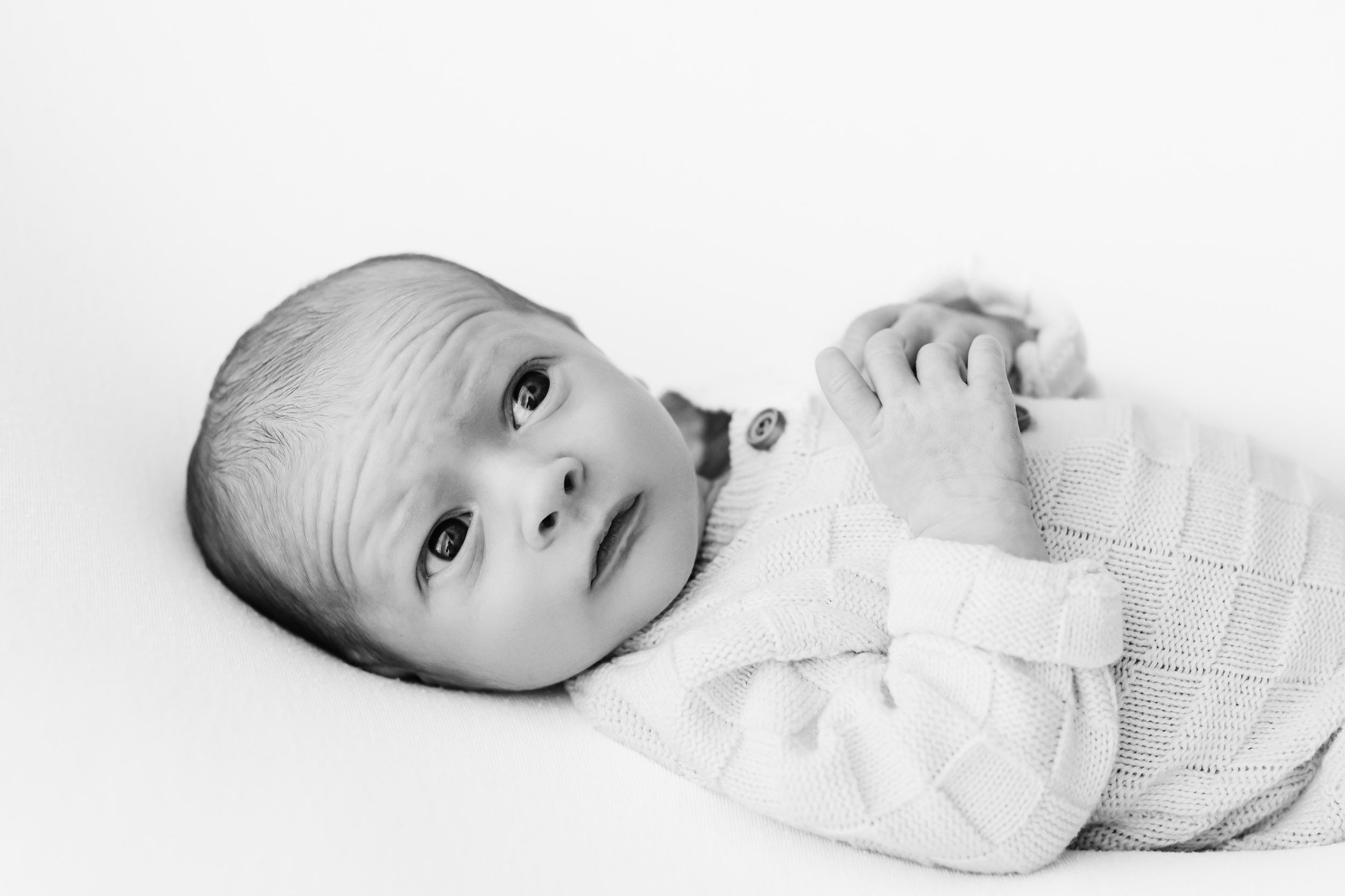 a timeless black and white image of a baby boy laying on his back and looking up toward the ceiling with catch lights in his eyes during a  newborn photoshoot