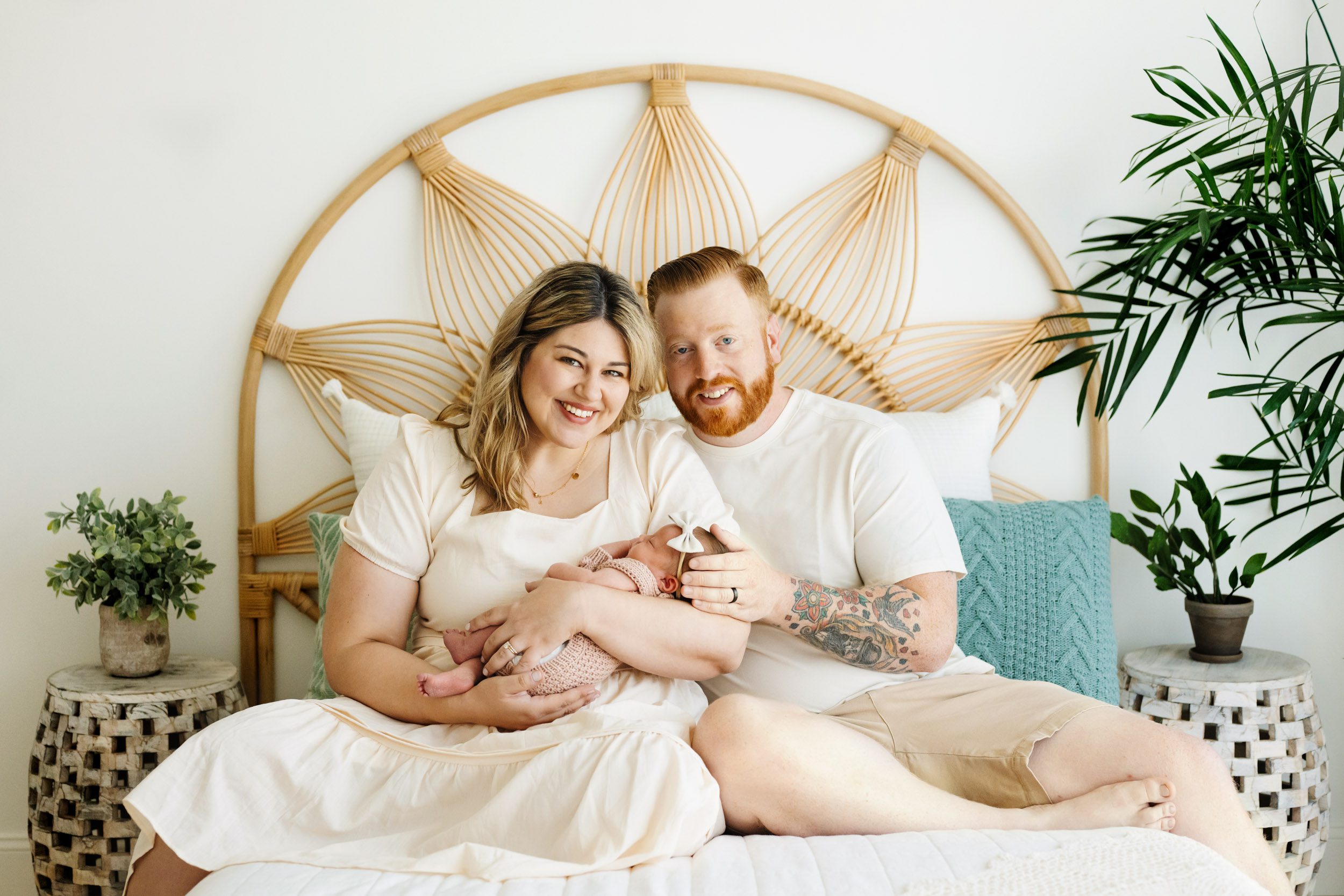 new parents sitting on a bed and holding their baby girl in their arms as they smile at the camera during a newborn photography session