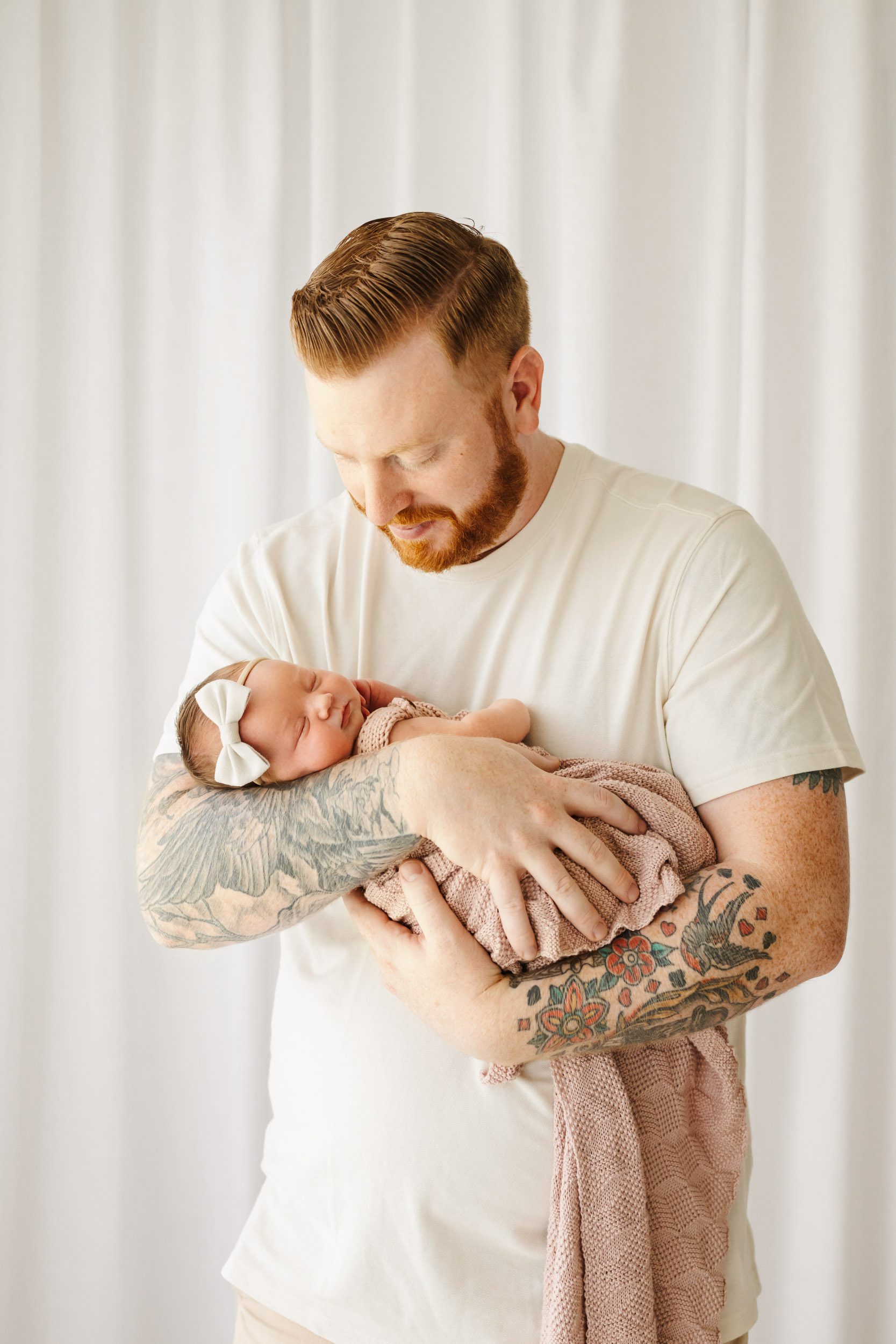 a father holding his newborn baby girl in his arms and smiling down at her during a newborn photography session
