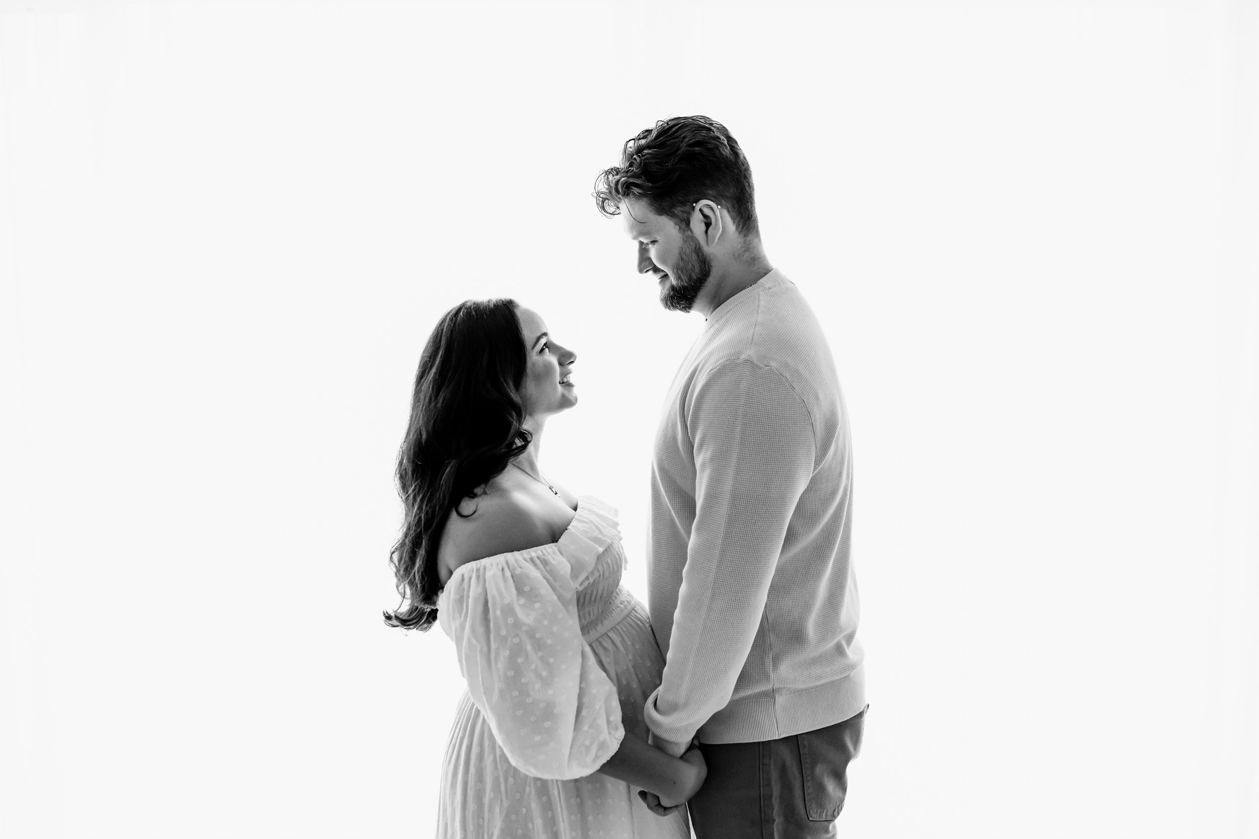 a monochrome backlit image of expectant parents clasping hands and gazing at one another during a lifestyle maternity photoshoot