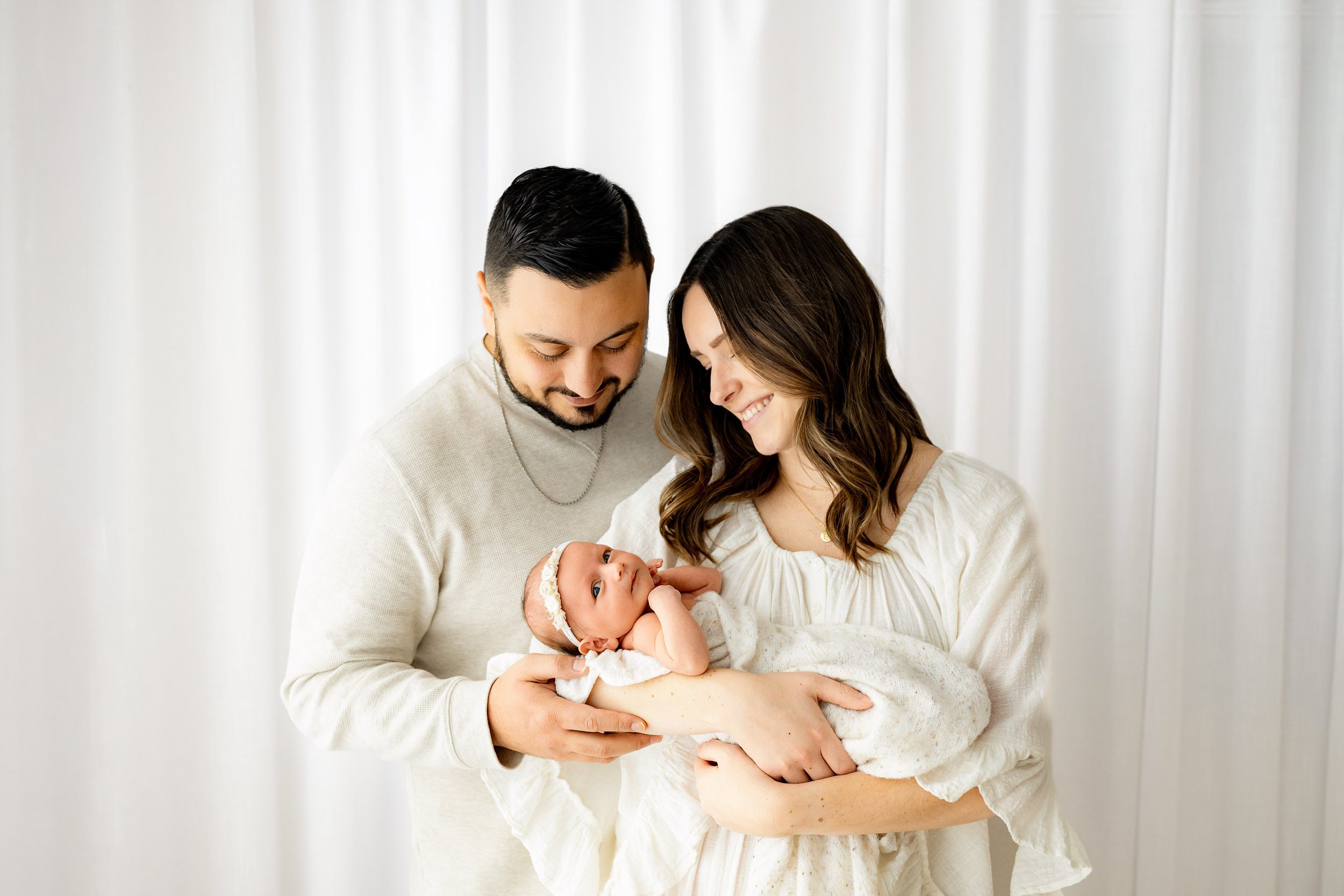 new parents cradling their baby girl in the arms and smiling down at her during a newborn baby photography session