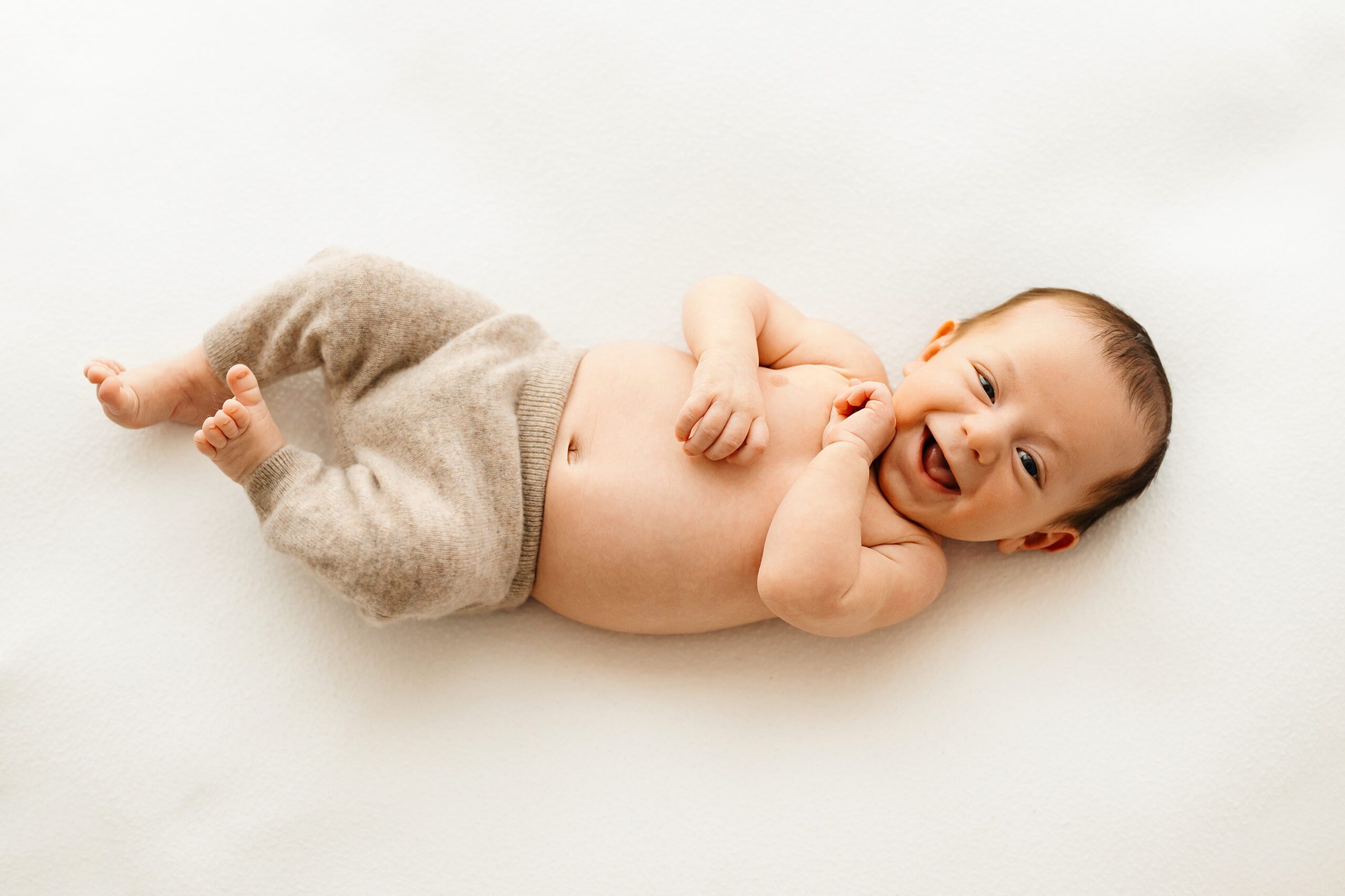 a baby boy laying in a white backdrop and smiling up at the camera during a Pottstown newborn photography photoshoot