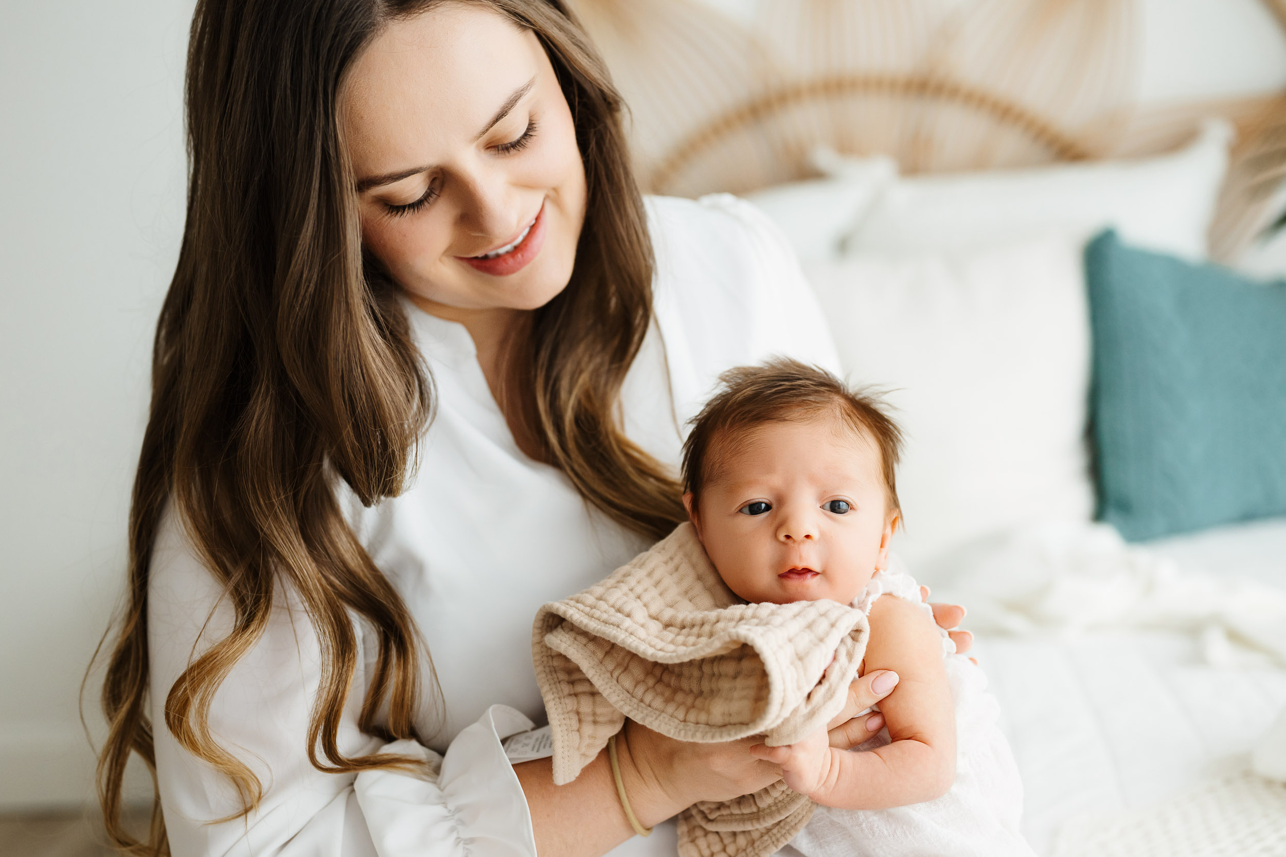 a new mom holding her baby girl in her arms and holding a burp cloth under her chin as she taps the baby's back to help her burp during a lifestyle newborn photoshoot